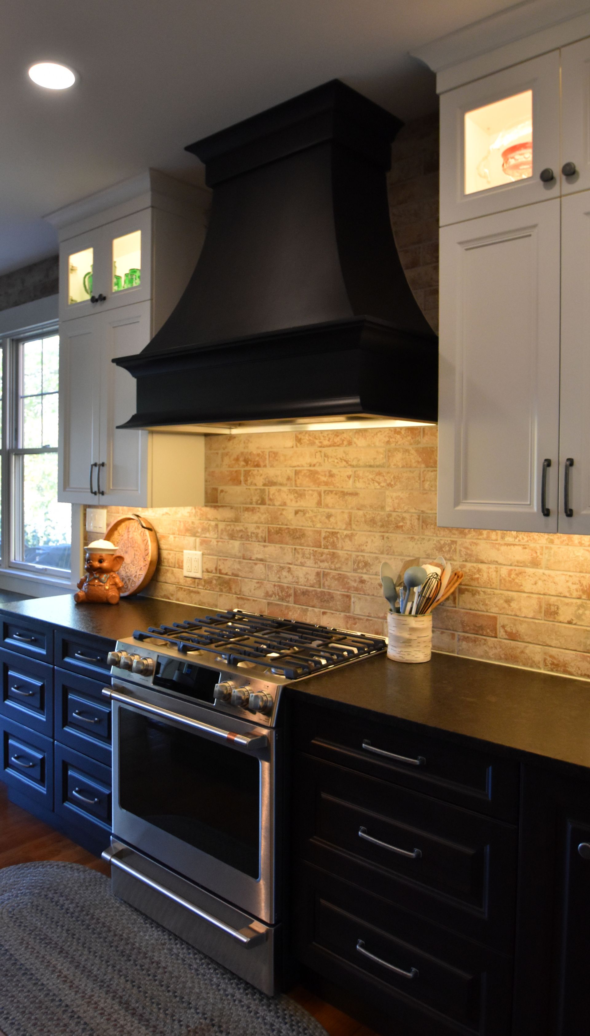 Modern kitchen with black stove, dark range hood, white cabinets, and tan tile backsplash