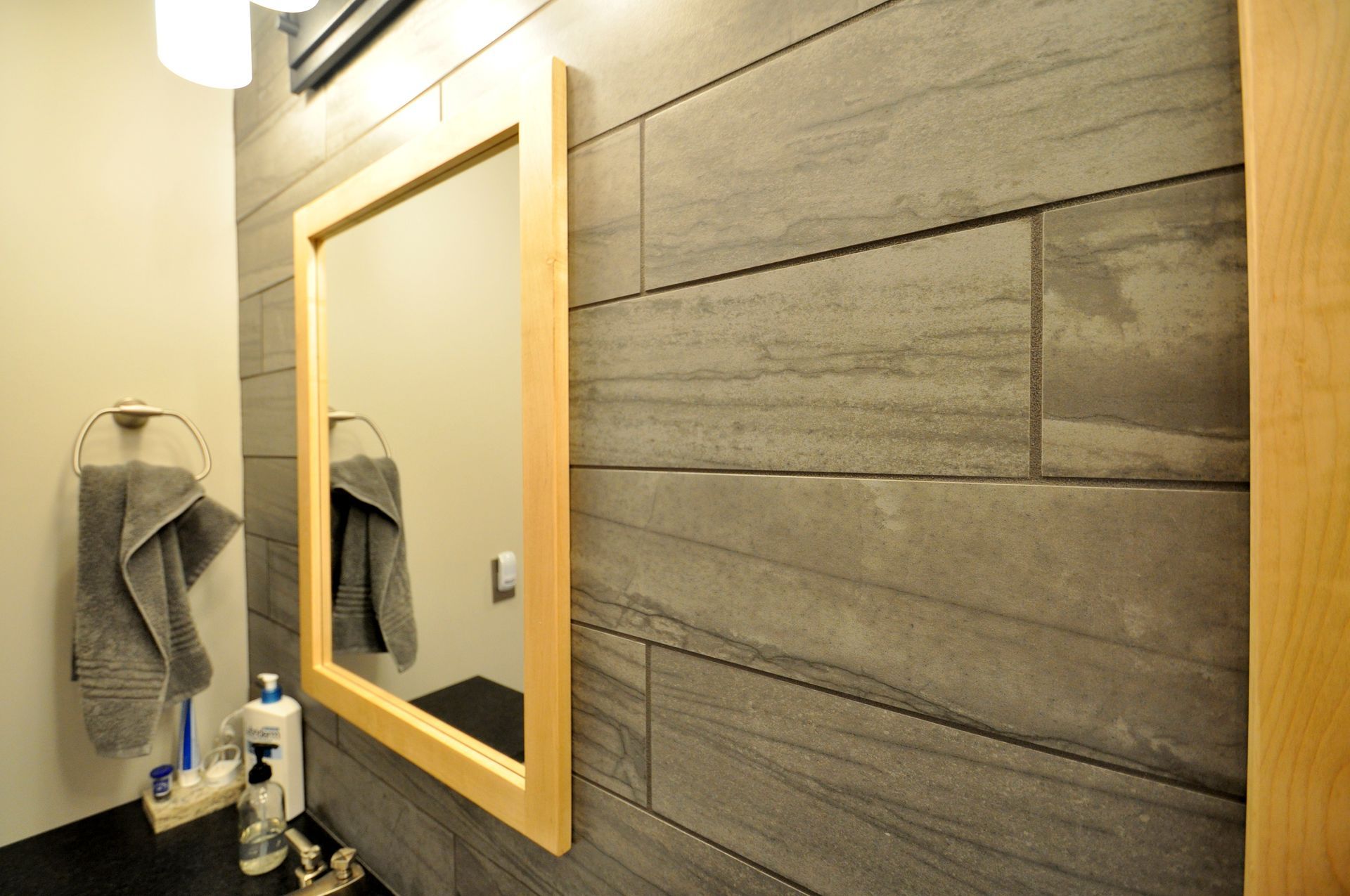 Bathroom vanity with wood-framed mirror, gray towel, and textured gray wall tiles