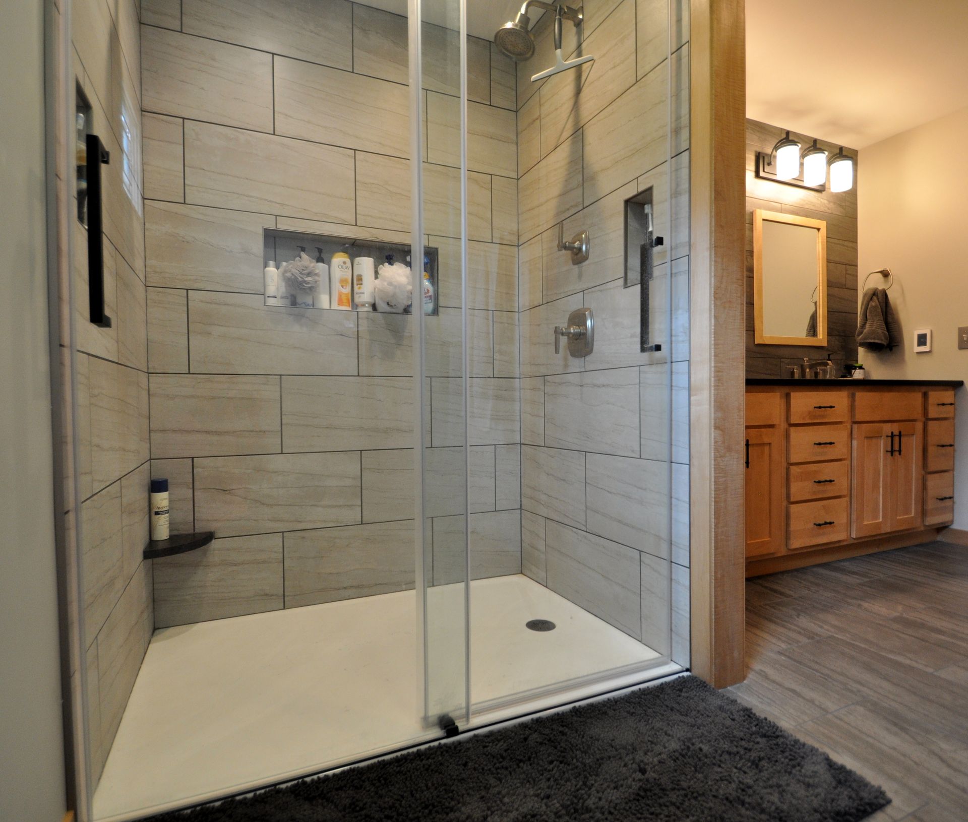 Modern bathroom with glass-enclosed shower, gray tile, and a wood vanity with mirror.