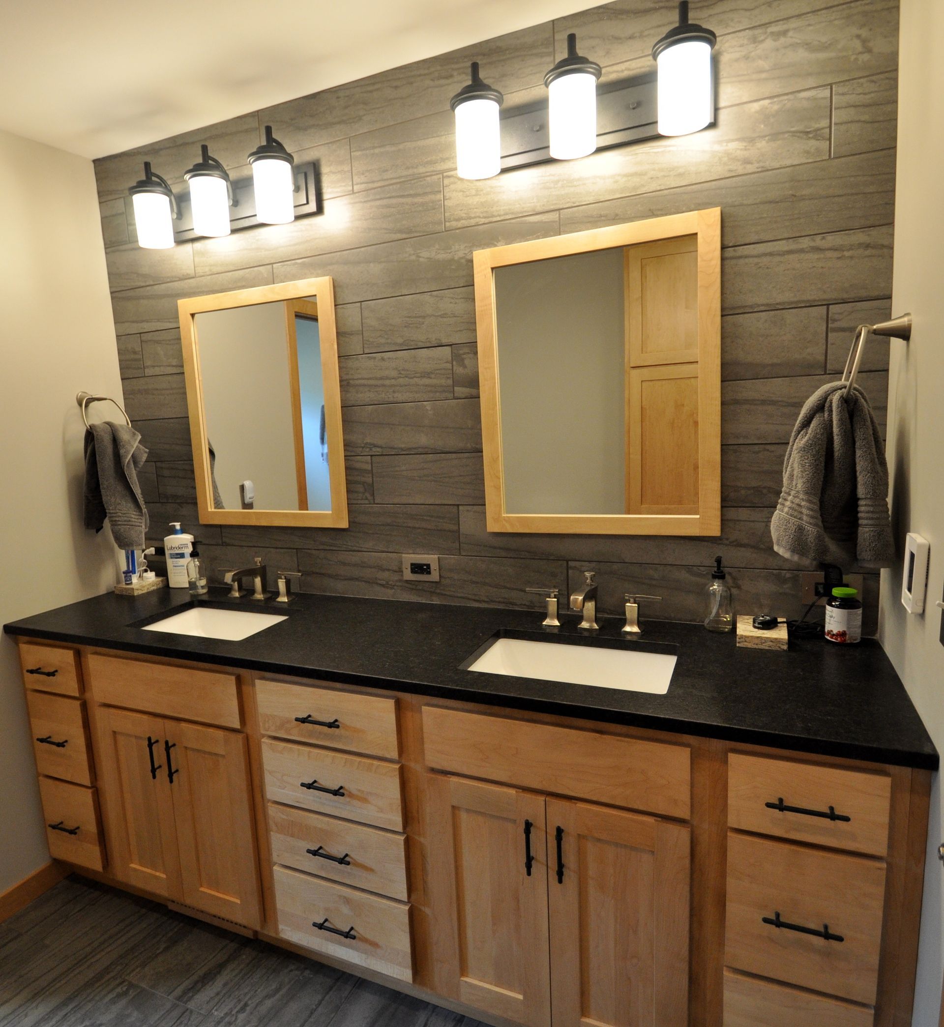 Wood vanity with black countertop, double mirrors, and wall sconces in a rustic bathroom.