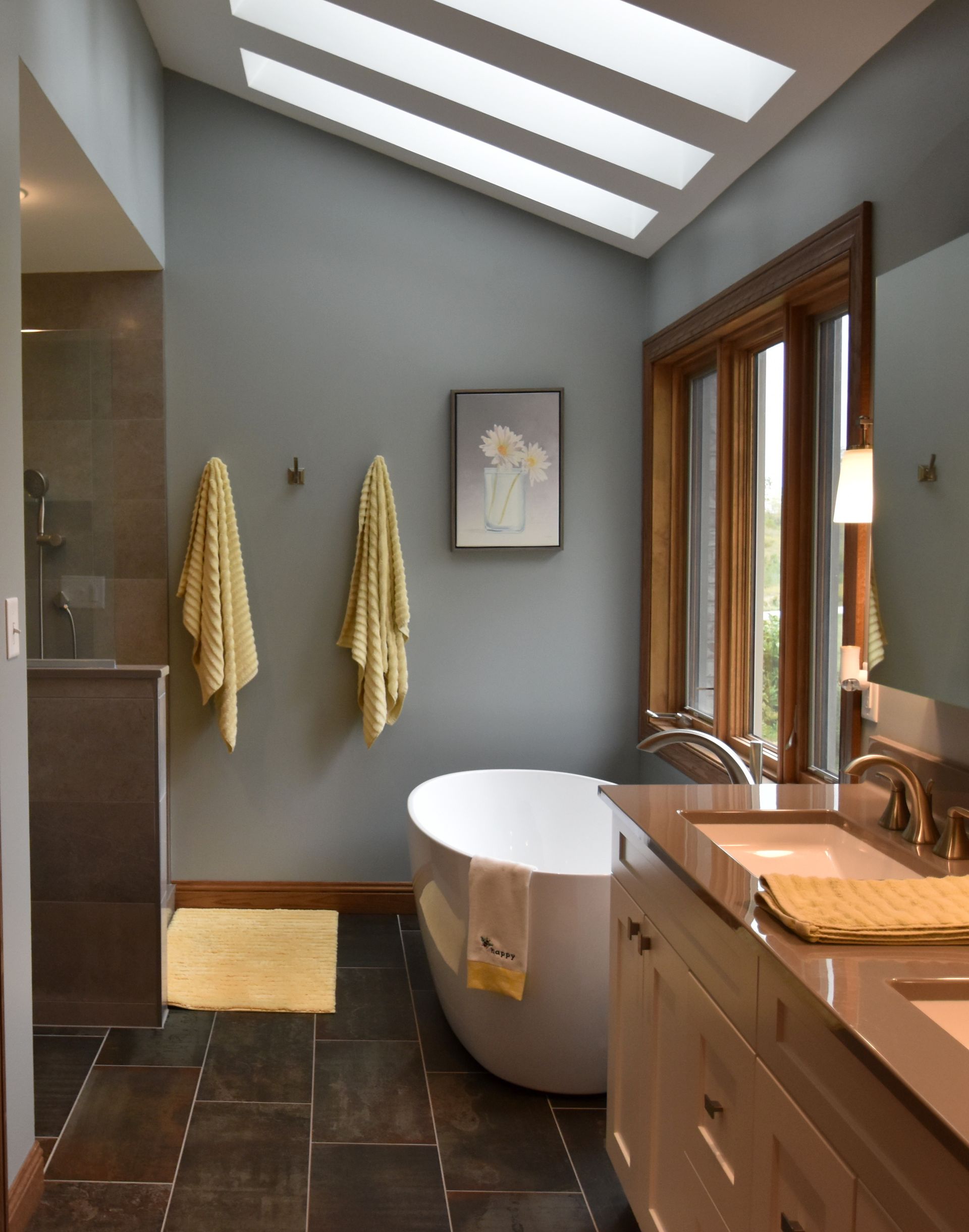 Modern bathroom with skylights, freestanding tub, double vanity, and wood-framed windows