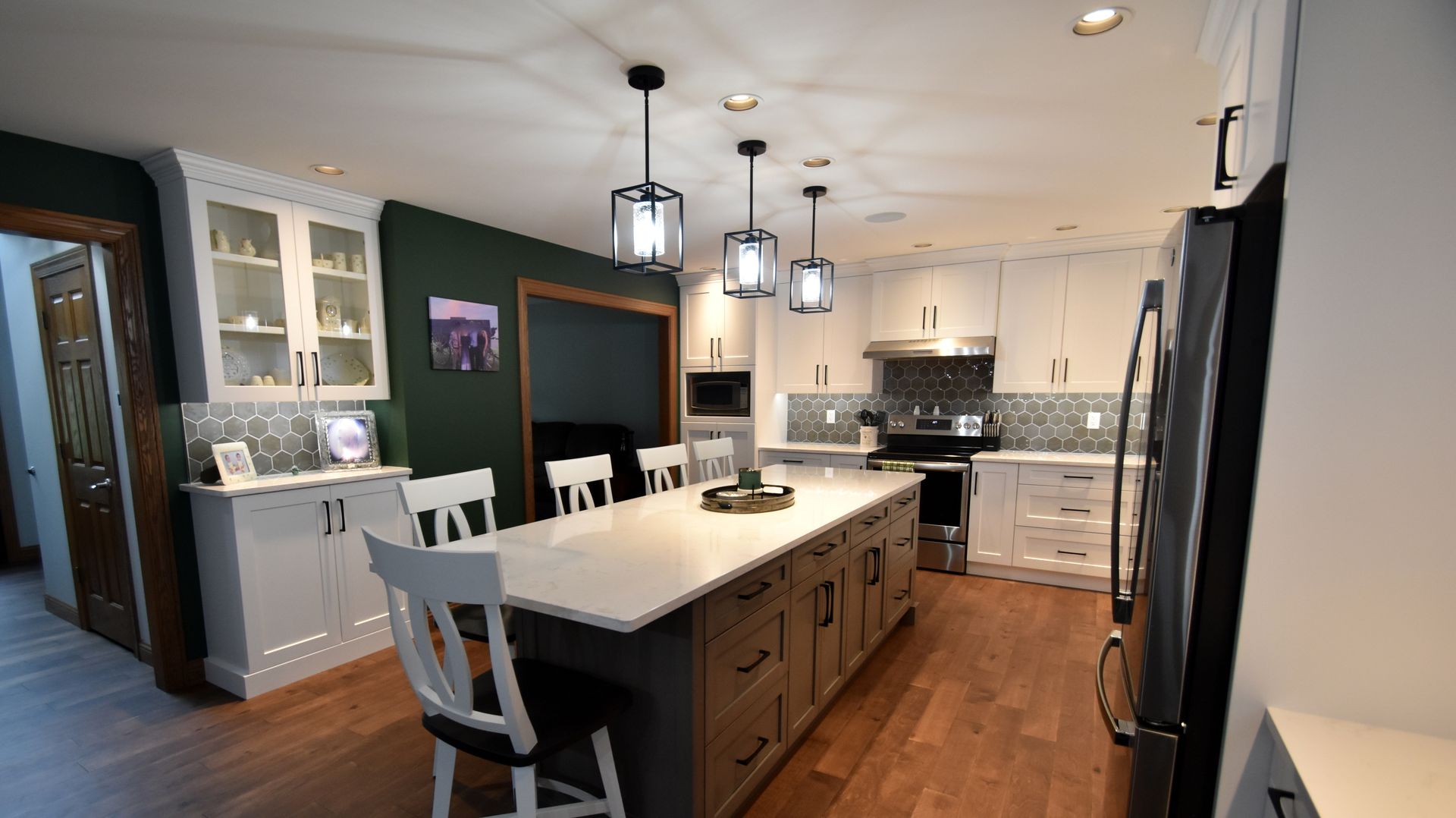 Bright modern kitchen with white cabinets, dark island, pendant lights, and hardwood floors