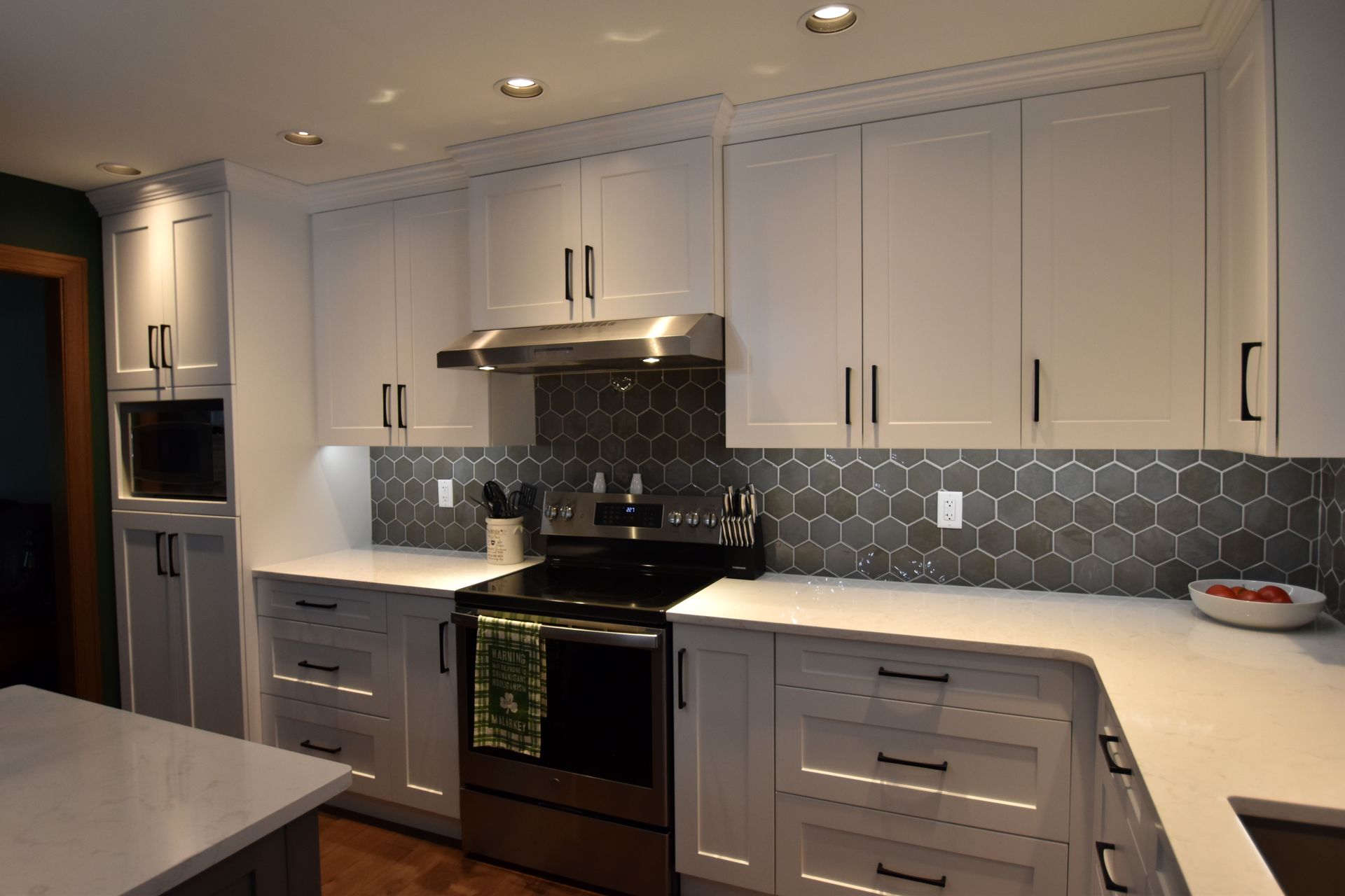 Modern kitchen with white cabinets, black backsplash, stainless appliances, and light countertops