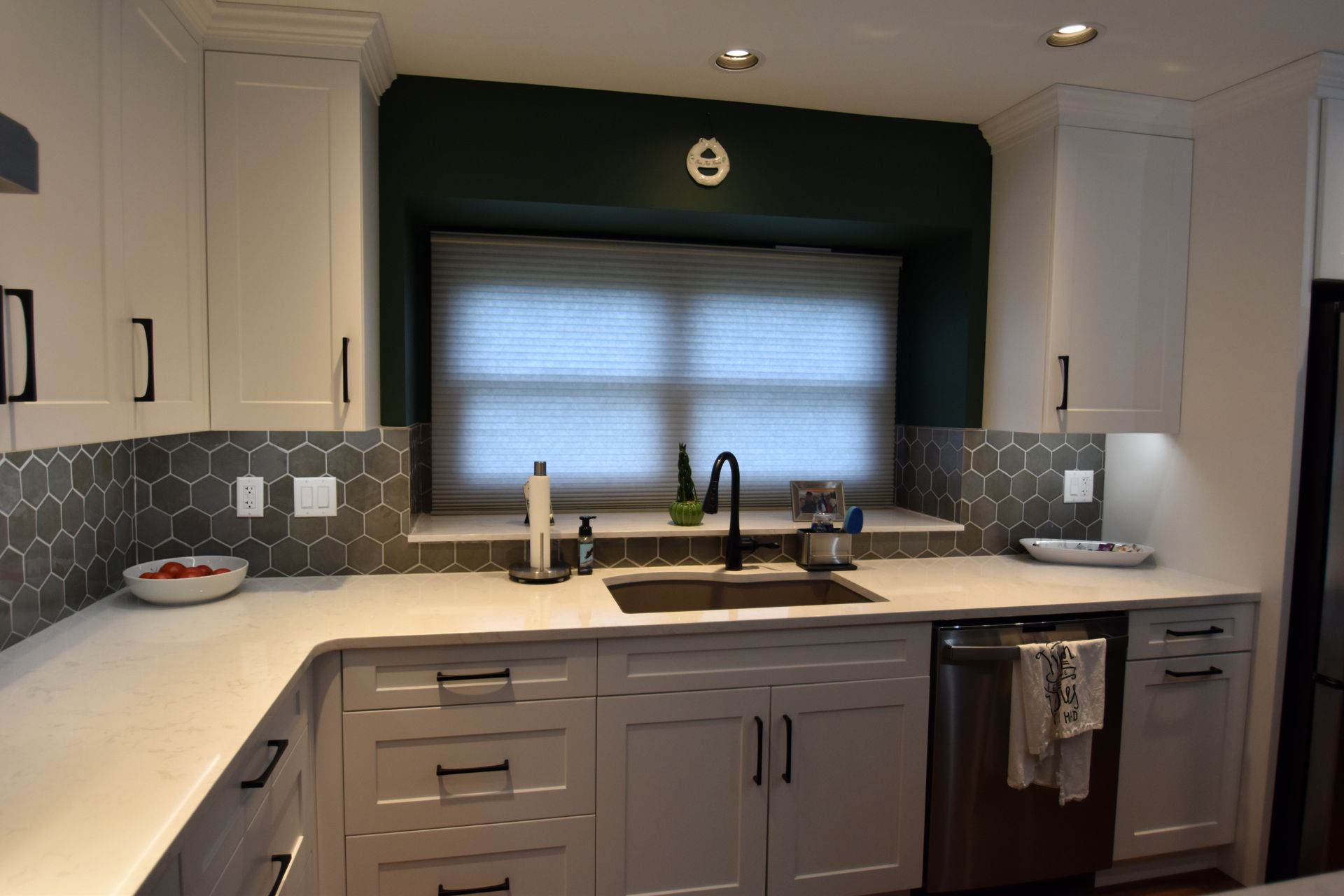 Modern kitchen with white cabinets, gray backsplash, and a window above the sink with a dark faucet.