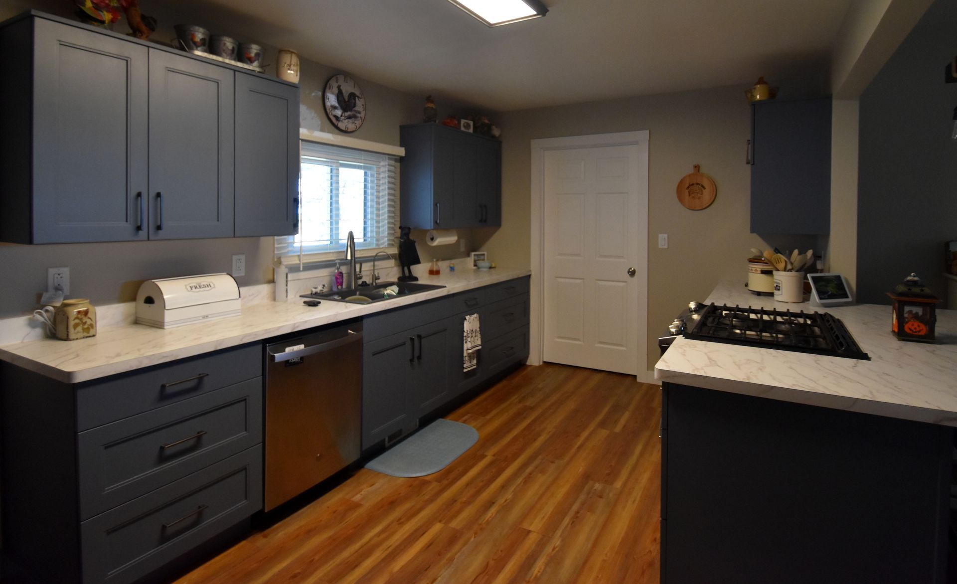 Blue kitchen with dark cabinets, white countertops, wood floors, and a gas stove by the window.