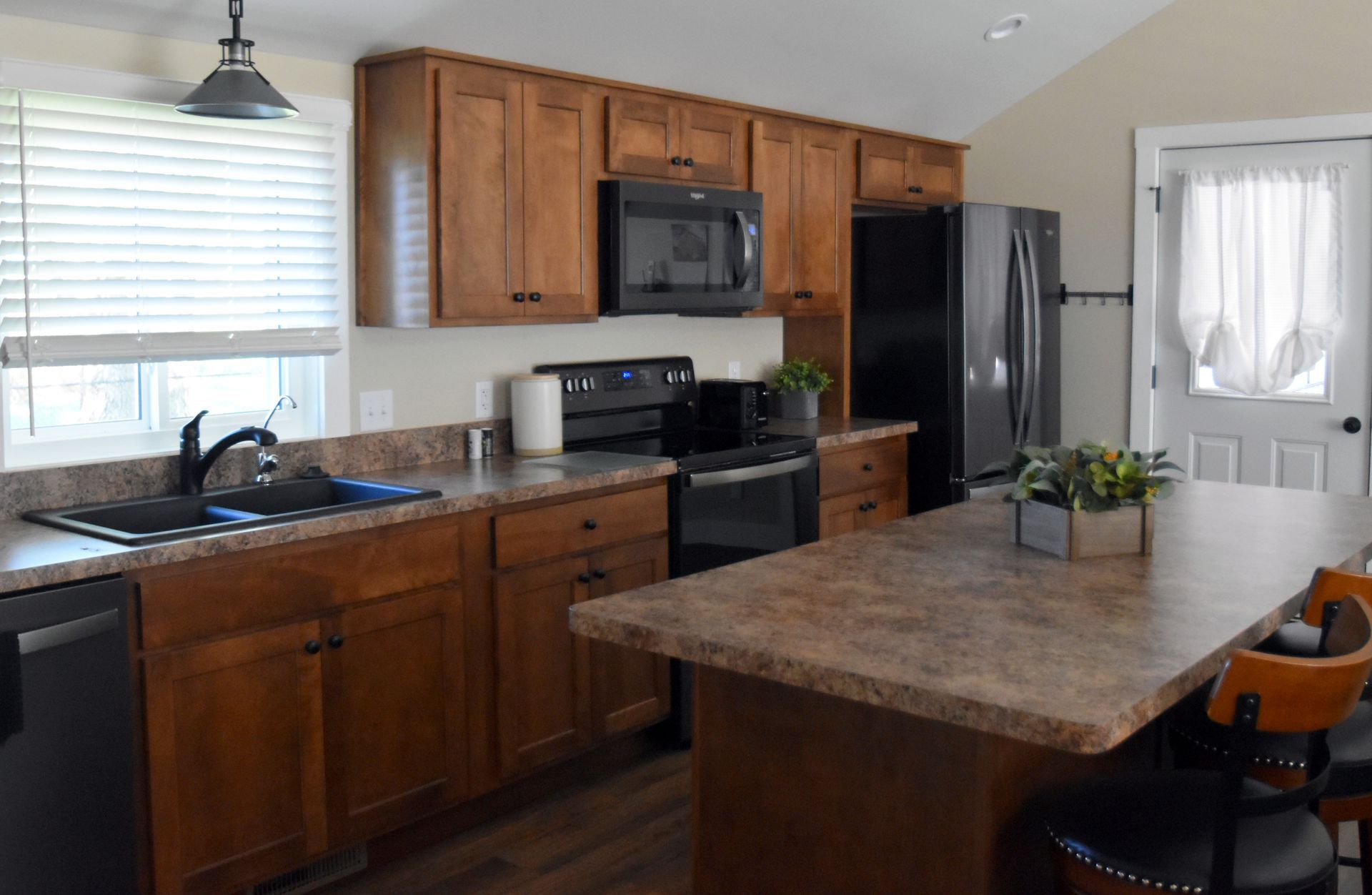 Modern kitchen with wood cabinets, black appliances, and a large island with stone countertop
