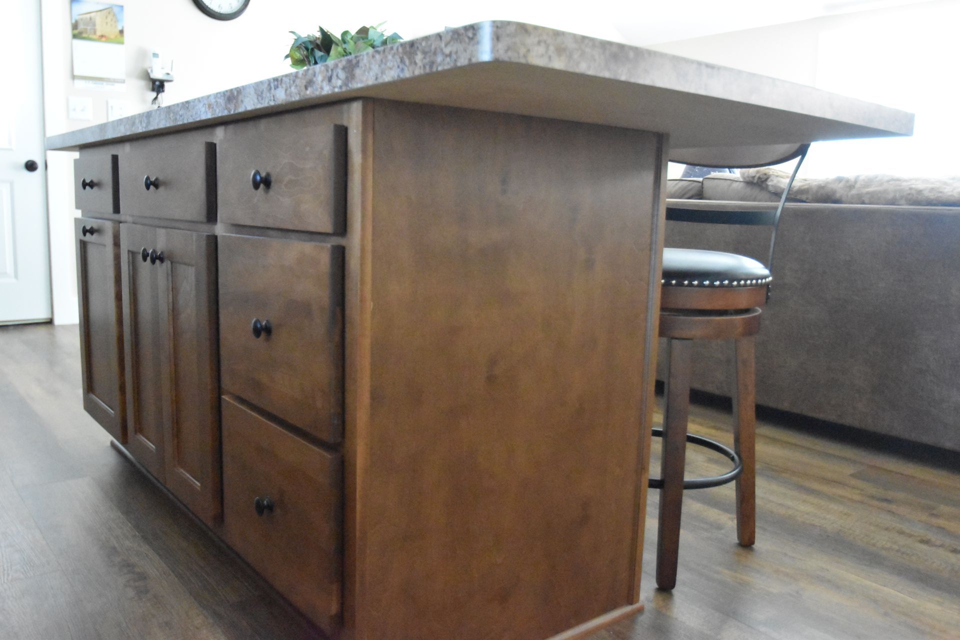 Wooden kitchen island with drawers and a granite countertop, shown beside a bar stool in a bright kitchen.