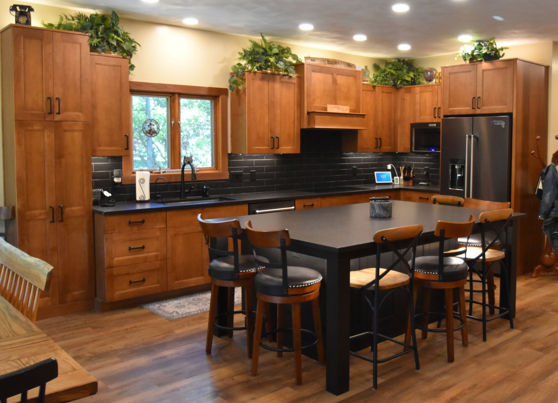 Modern kitchen with wood cabinets, black countertops, island, bar stools, and potted plants above cabinets
