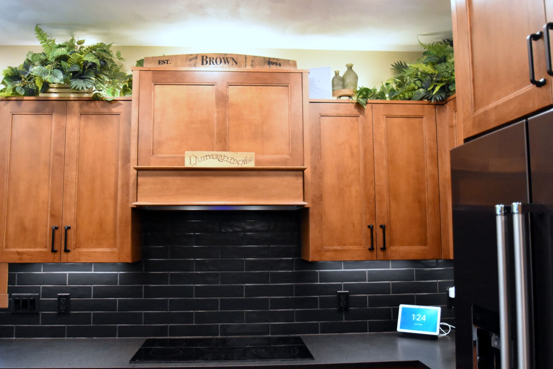 Modern kitchen with wooden cabinets, black tile backsplash, and countertop plants above the cabinets