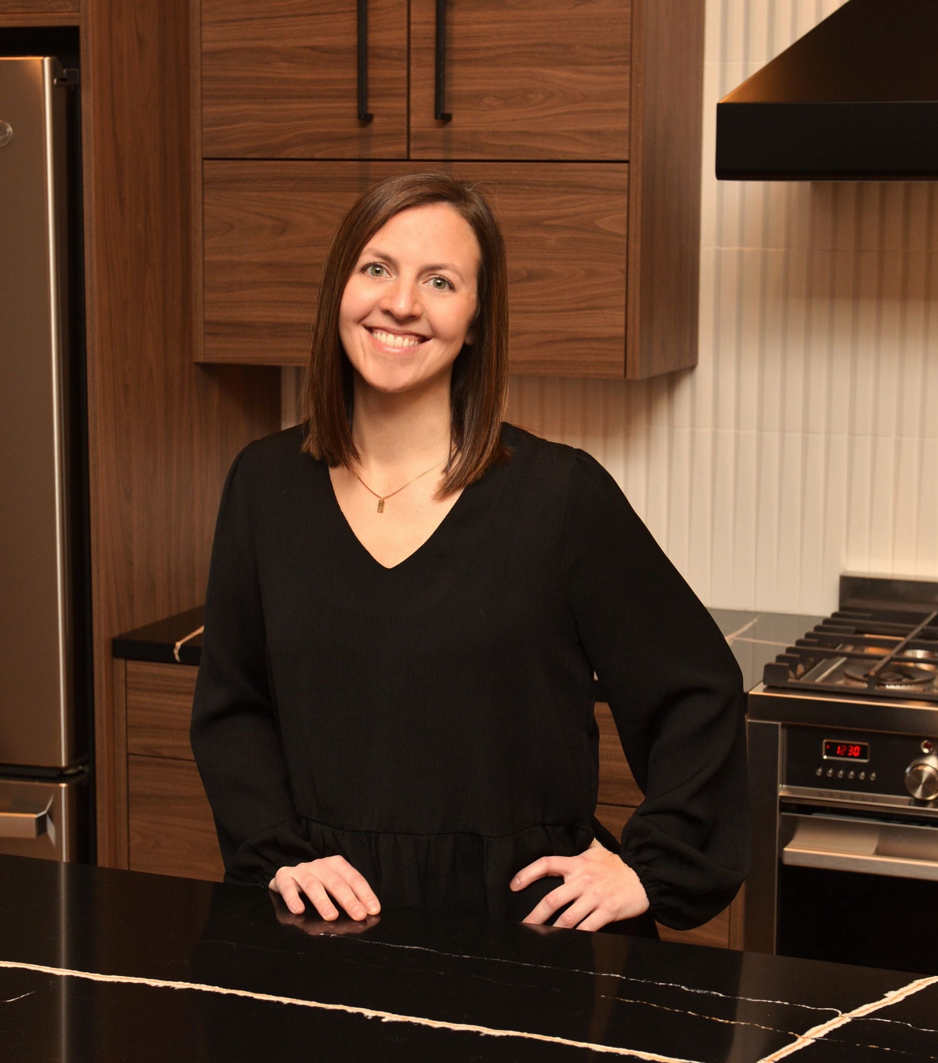 Smiling woman in a black sweater standing in a kitchen beside a dark countertop