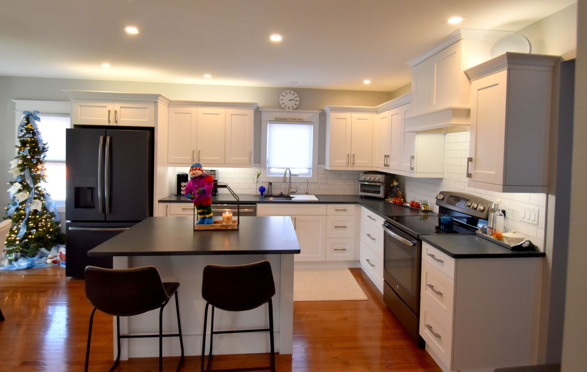 Bright modern kitchen with white cabinets, black island, bar stools, and a small decorated Christmas tree