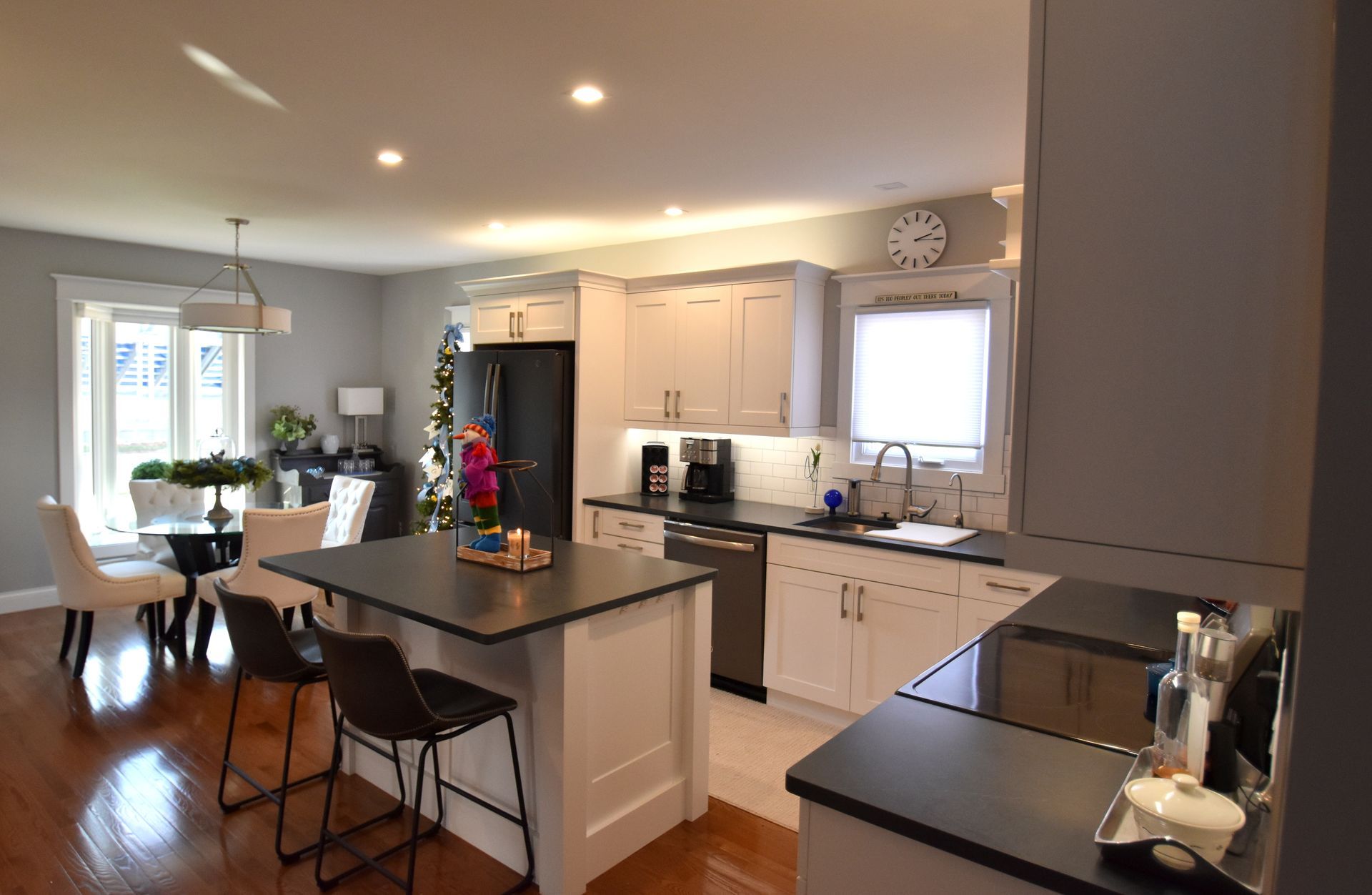 Bright modern kitchen with island, bar stools, white cabinets, hardwood floors, and small dining nook