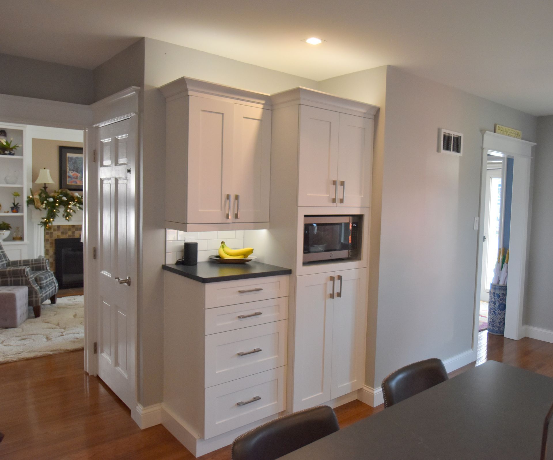 Bright kitchen with white cabinets, black countertops, and a bowl of bananas beside a dining area.