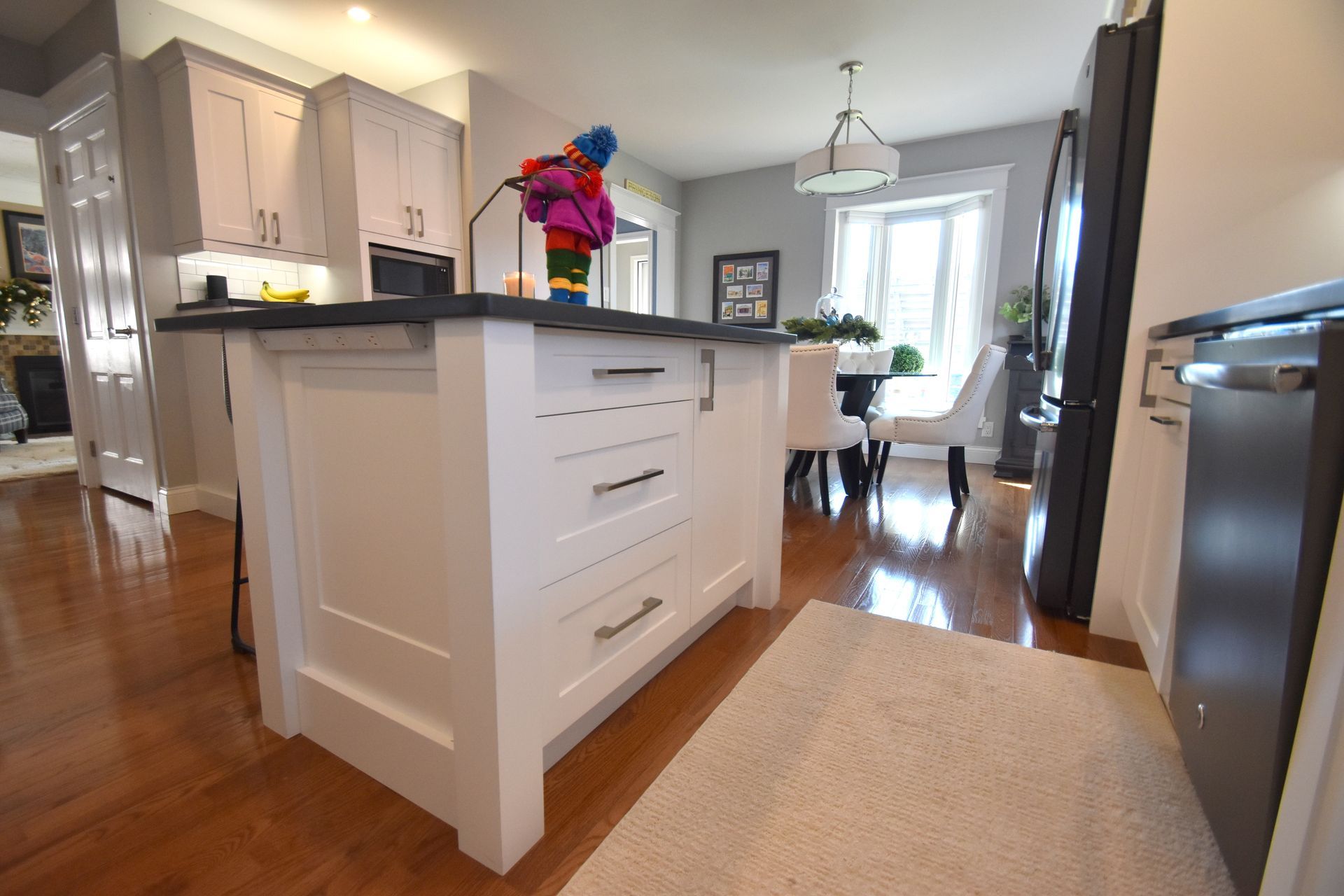 Bright kitchen with white island, hardwood floors, dining table, and colorful flowers by a sunlit window