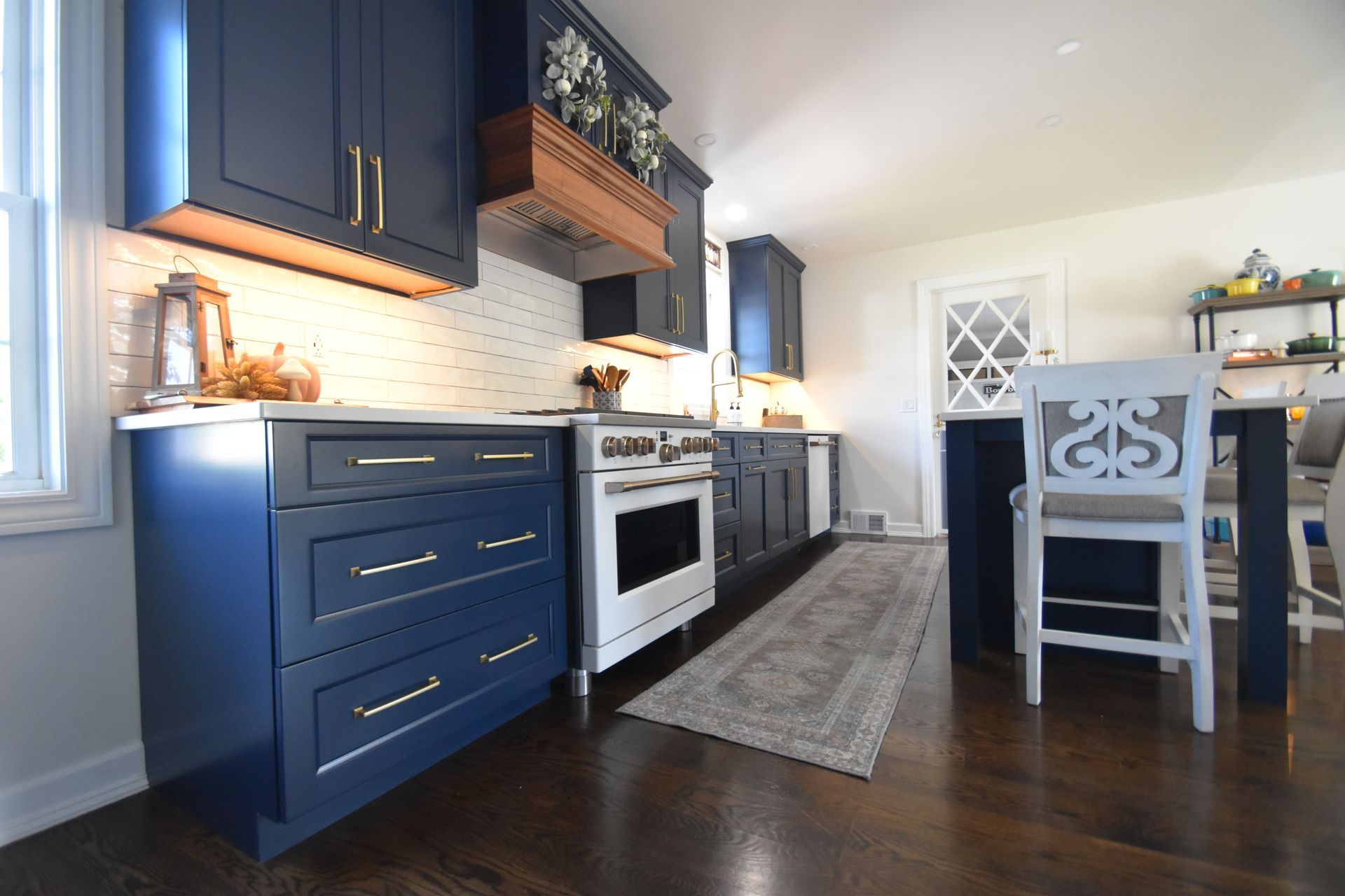 Modern kitchen with navy cabinets, white appliances, wood shelves, and a dining table on dark floors