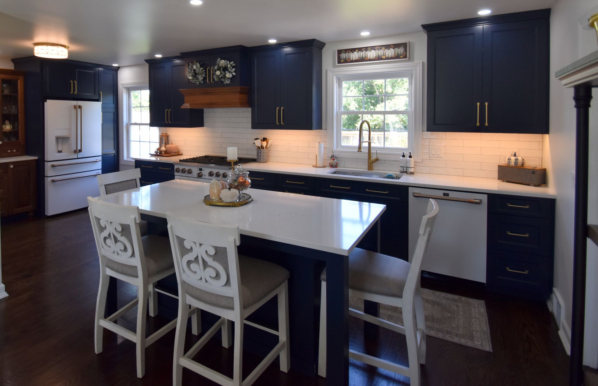 Modern kitchen with dark cabinets, white island, and two white bar stools by a window.