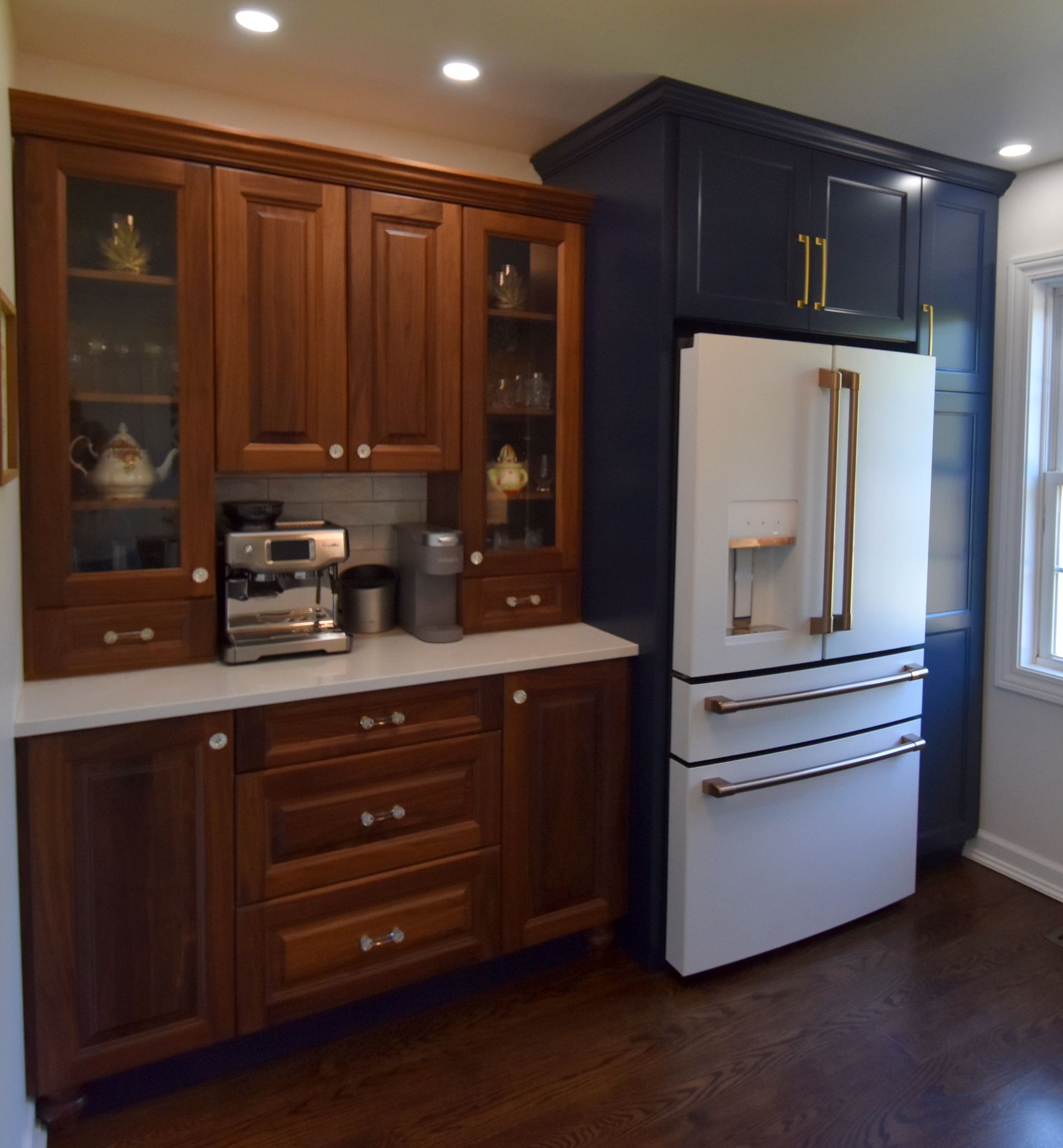 Kitchen with dark wood cabinets, white countertops, and a stainless steel refrigerator in a bright corner.