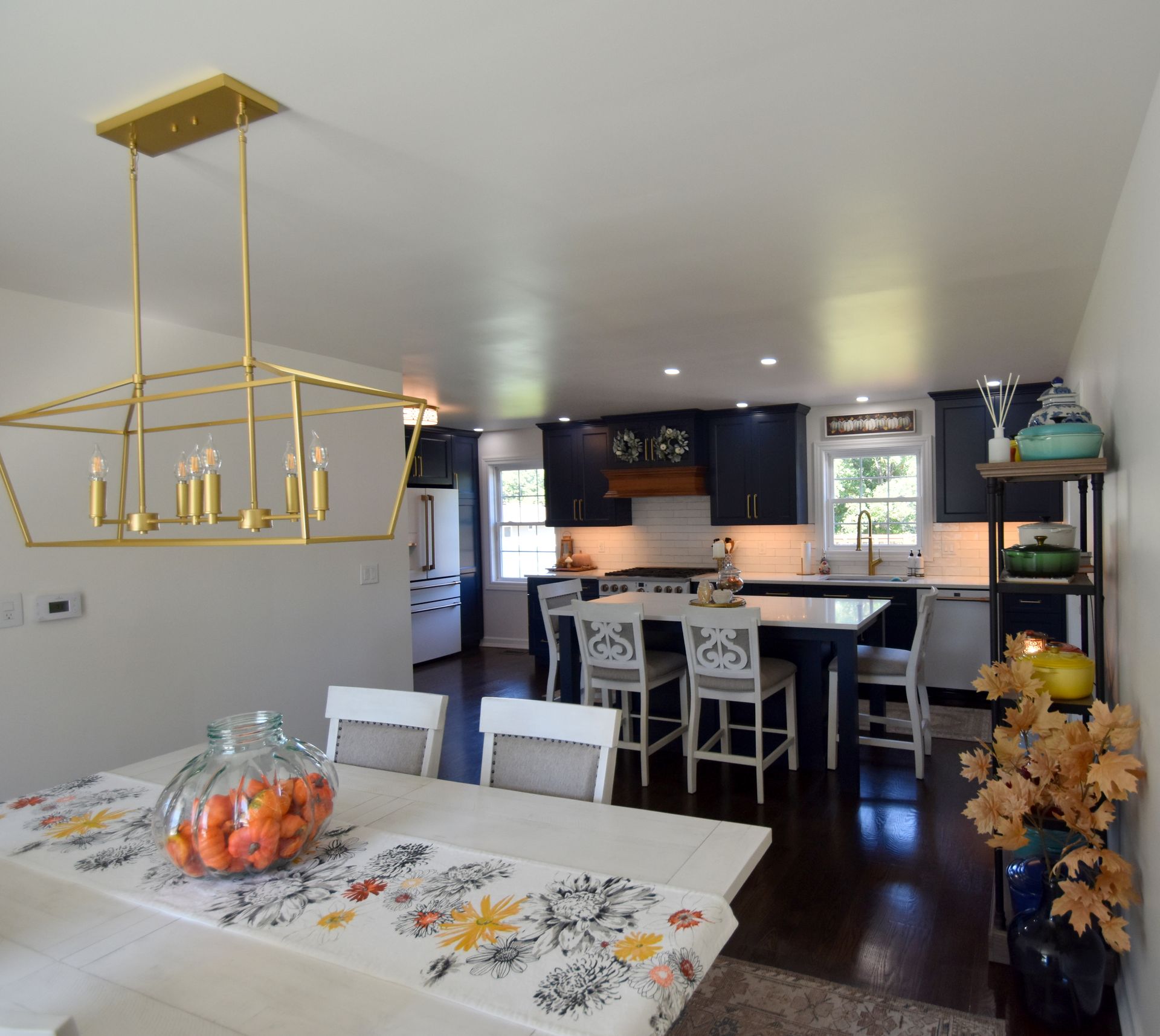 Bright dining and kitchen area with white table, gold chandelier, dark cabinets, and fruit bowl on the table