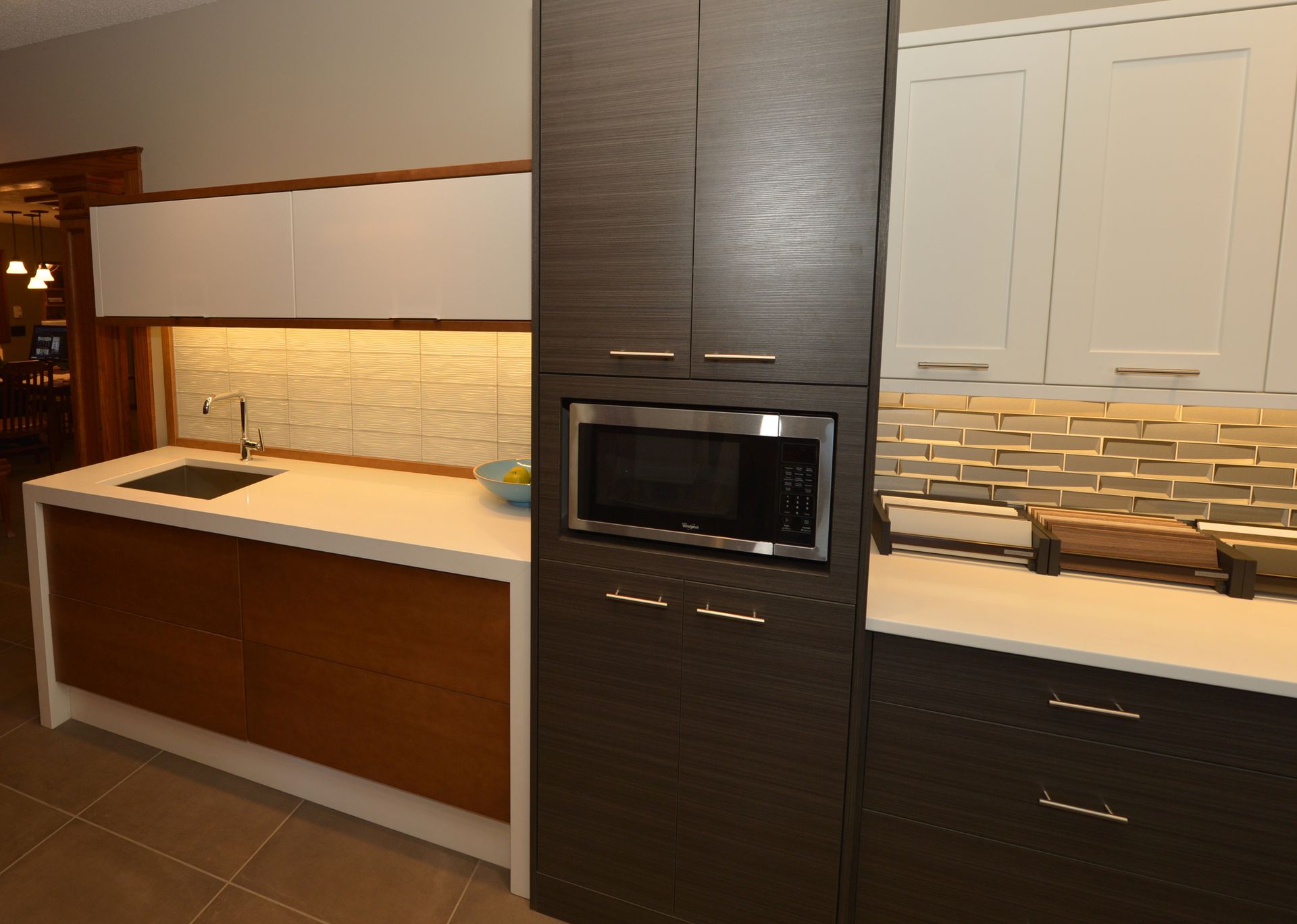 Modern kitchen with white and dark wood cabinets, stone backsplash, and built-in microwave