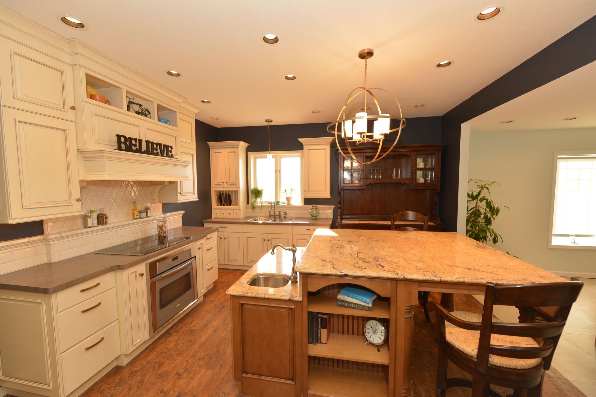 Bright kitchen with white cabinets, granite island, and hardwood floors under warm pendant lights