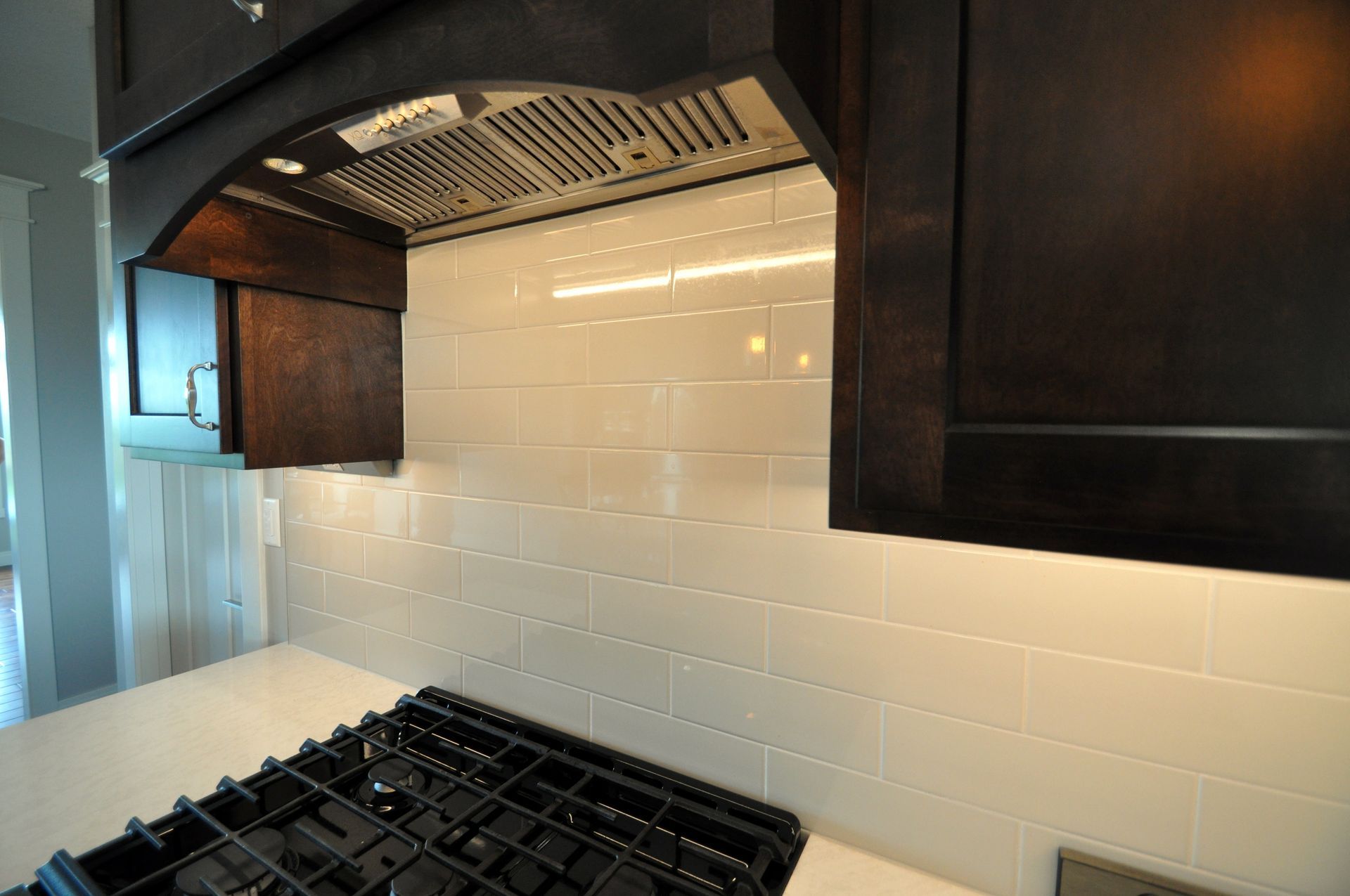 Modern kitchen with gas stove, white tile backsplash, and stainless steel range hood