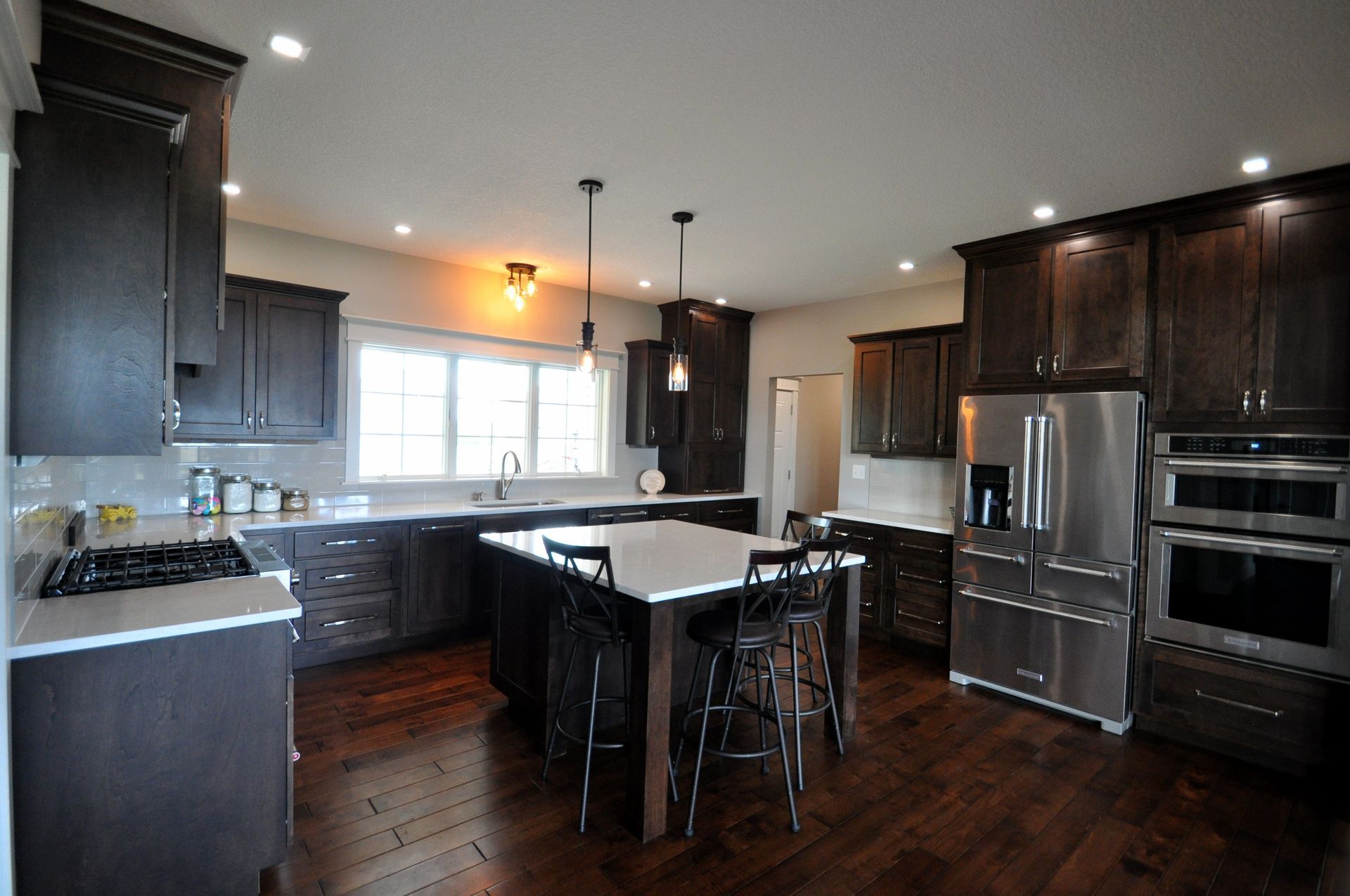 Modern kitchen with dark wood cabinets, stainless steel appliances, and a central island under pendant lights