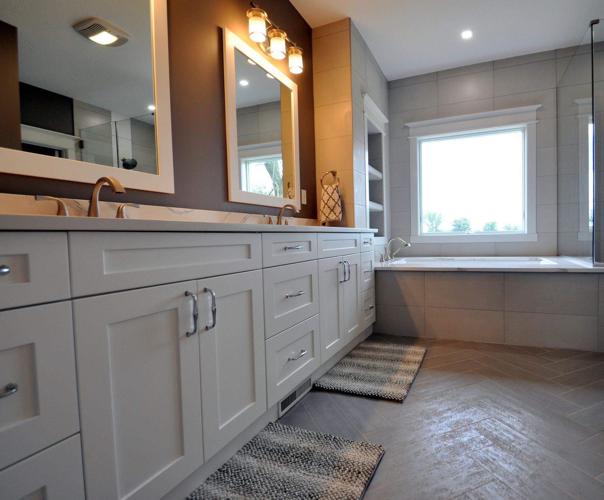 Modern bathroom with white vanity, large mirror, and bright window over a tiled tub area