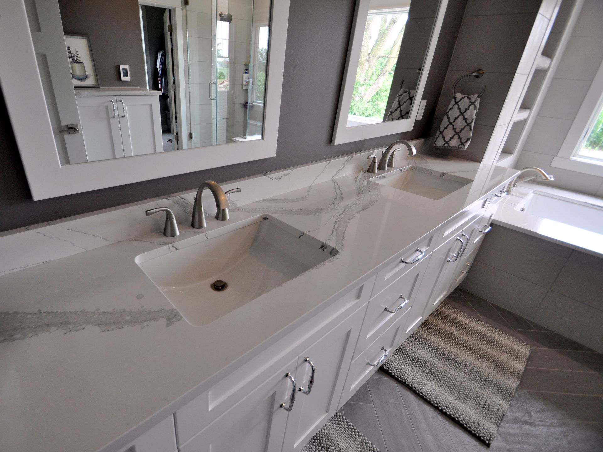 Bright white bathroom vanity with double sinks, large mirror, and window beside a striped rug.