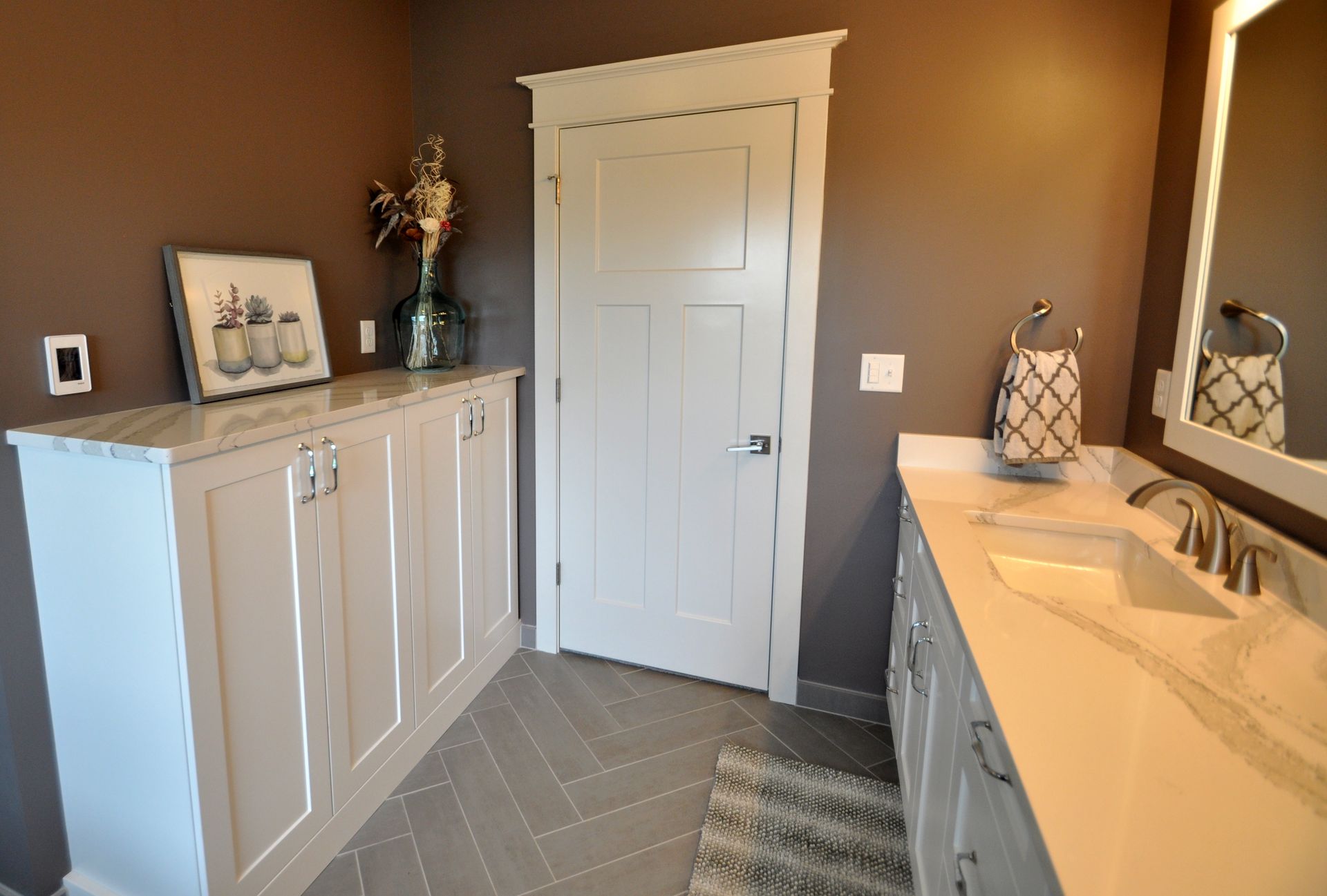 Bright bathroom with white vanity, cabinet, and door, brown walls, and striped rug.