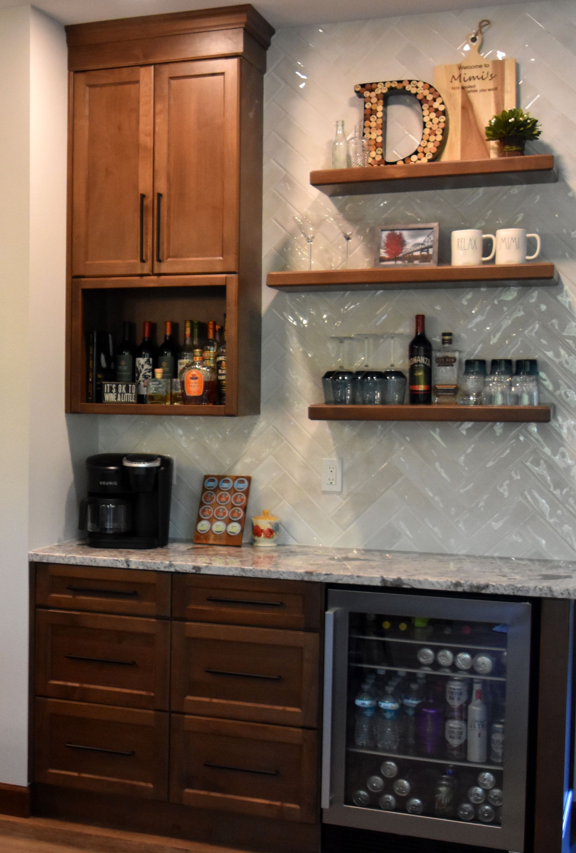 Home wet bar with wood cabinets, shelves of glassware and bottles, and a small wine fridge underneath.