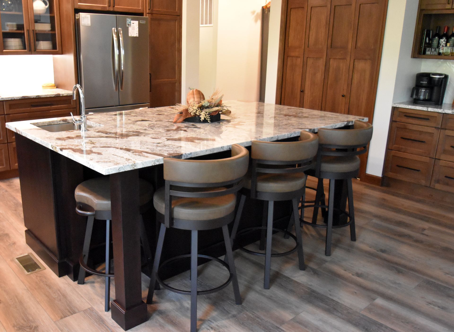Modern kitchen with a large marble island, four stools, stainless fridge, and wood cabinets