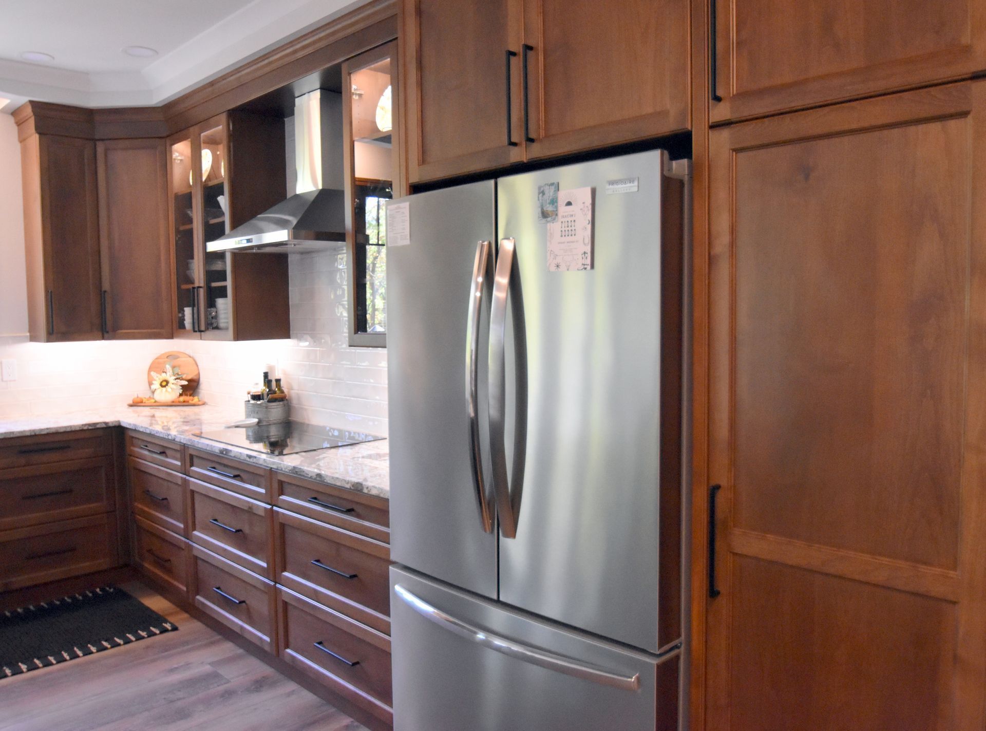 Modern kitchen with dark wood cabinets, stainless steel refrigerator, and light countertops.