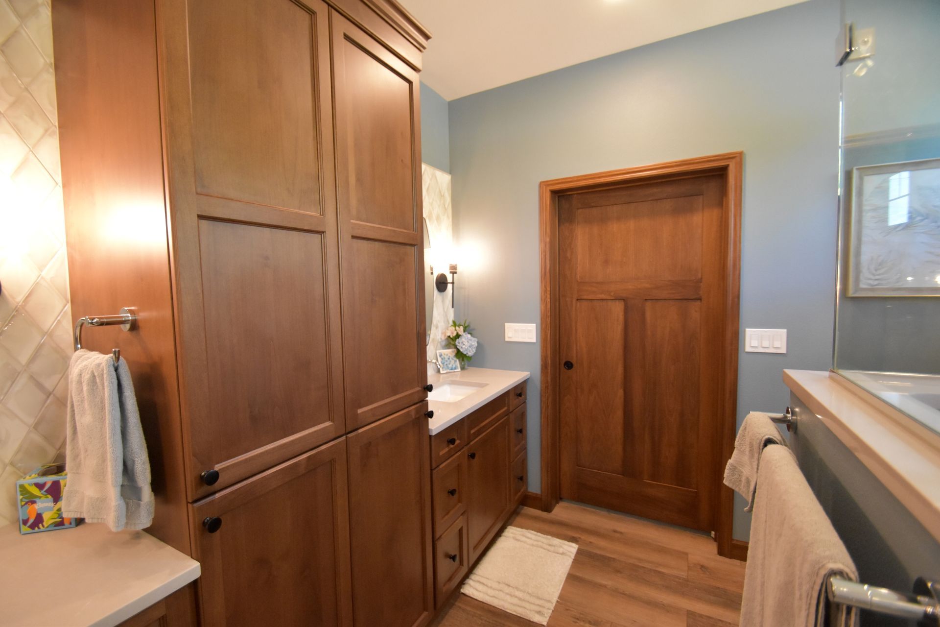 Bathroom with wood cabinets, white sink, blue walls, and a closed wooden door.