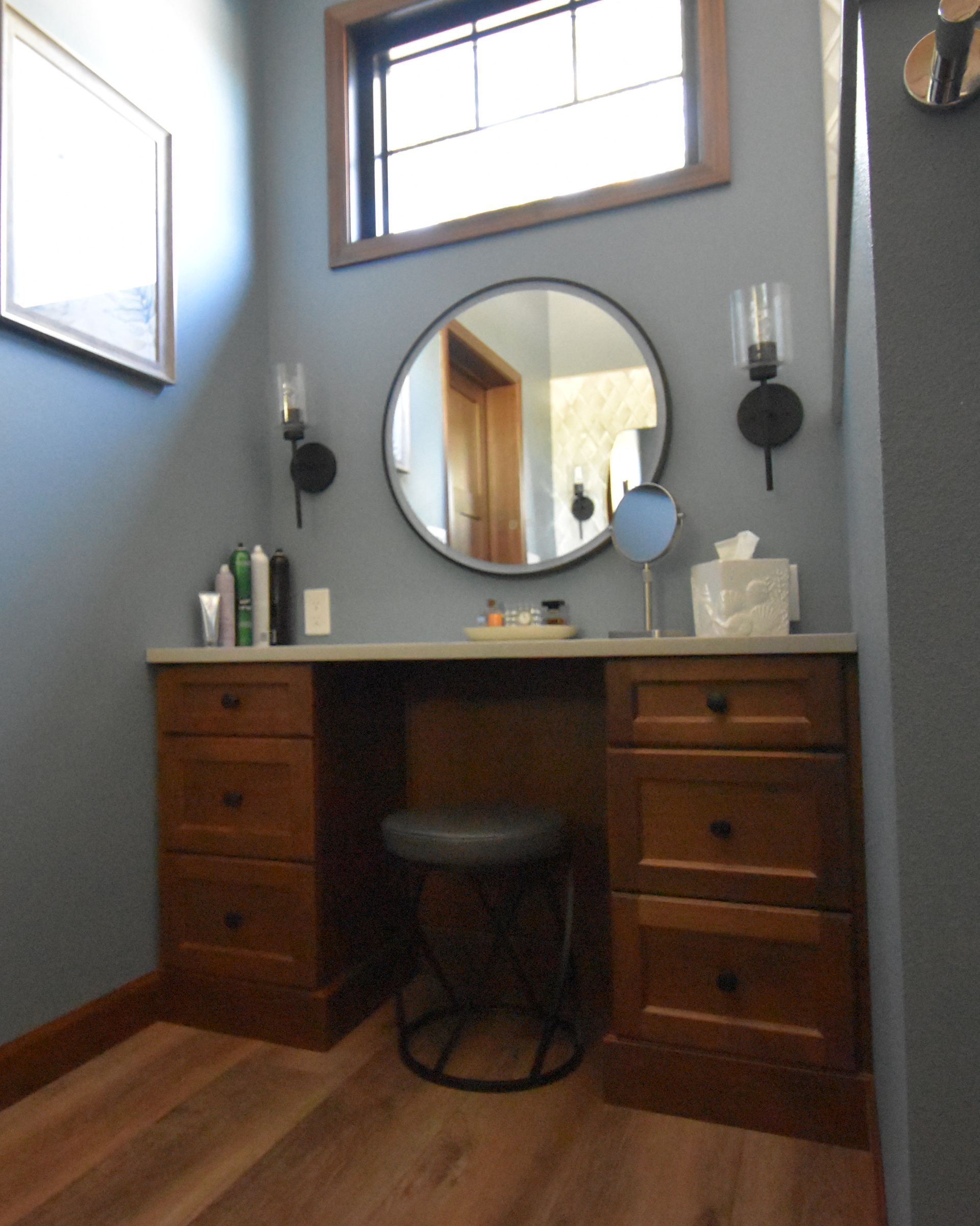 Wooden vanity desk with round mirror in a small bathroom, gray walls and wood floor