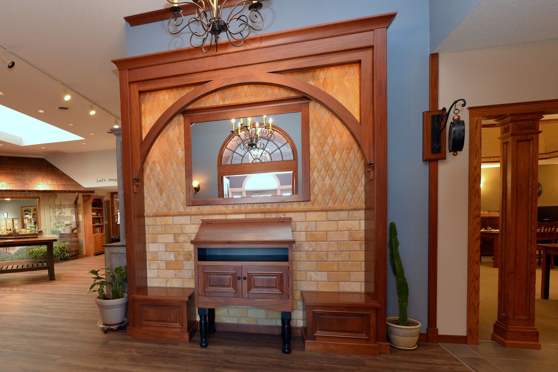 Wooden fireplace mantel with brick surround in a lobby or showroom, centered beneath an arched mirror.