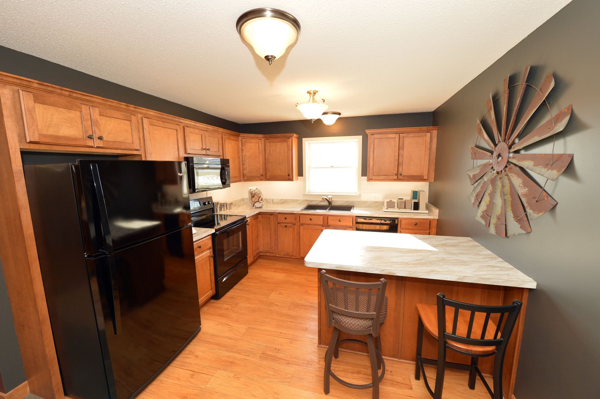 Kitchen with black appliances, wood cabinets, and a small island with two stools under ceiling lights