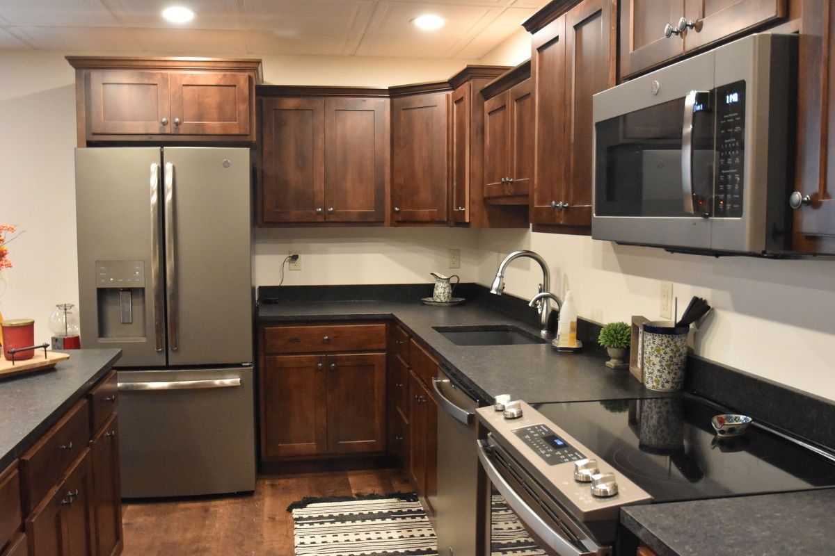 Compact kitchen with stainless steel appliances, dark wood cabinets, and black countertops.