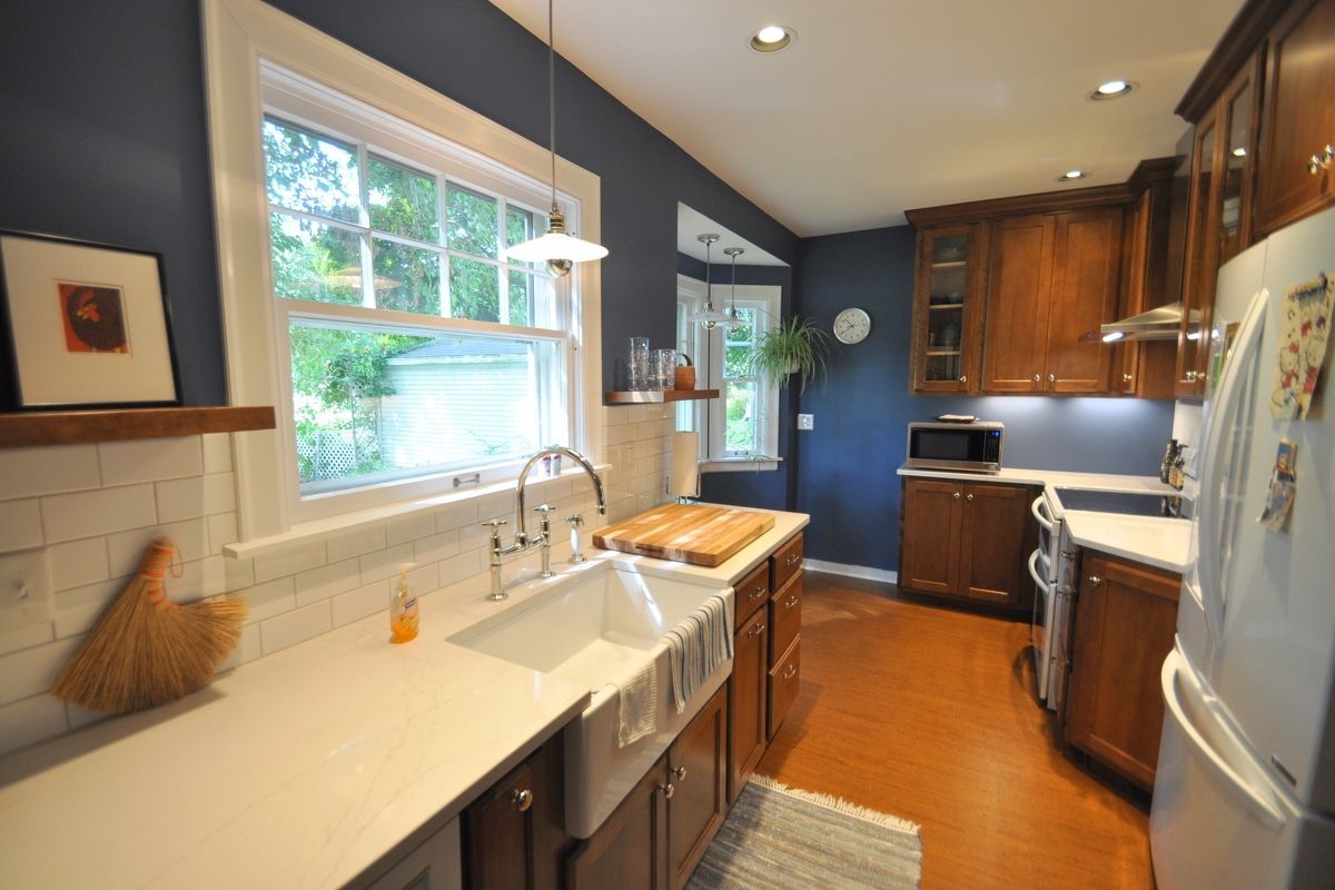 Bright kitchen with white countertops, wooden cabinets, window, and stainless sink and appliances.