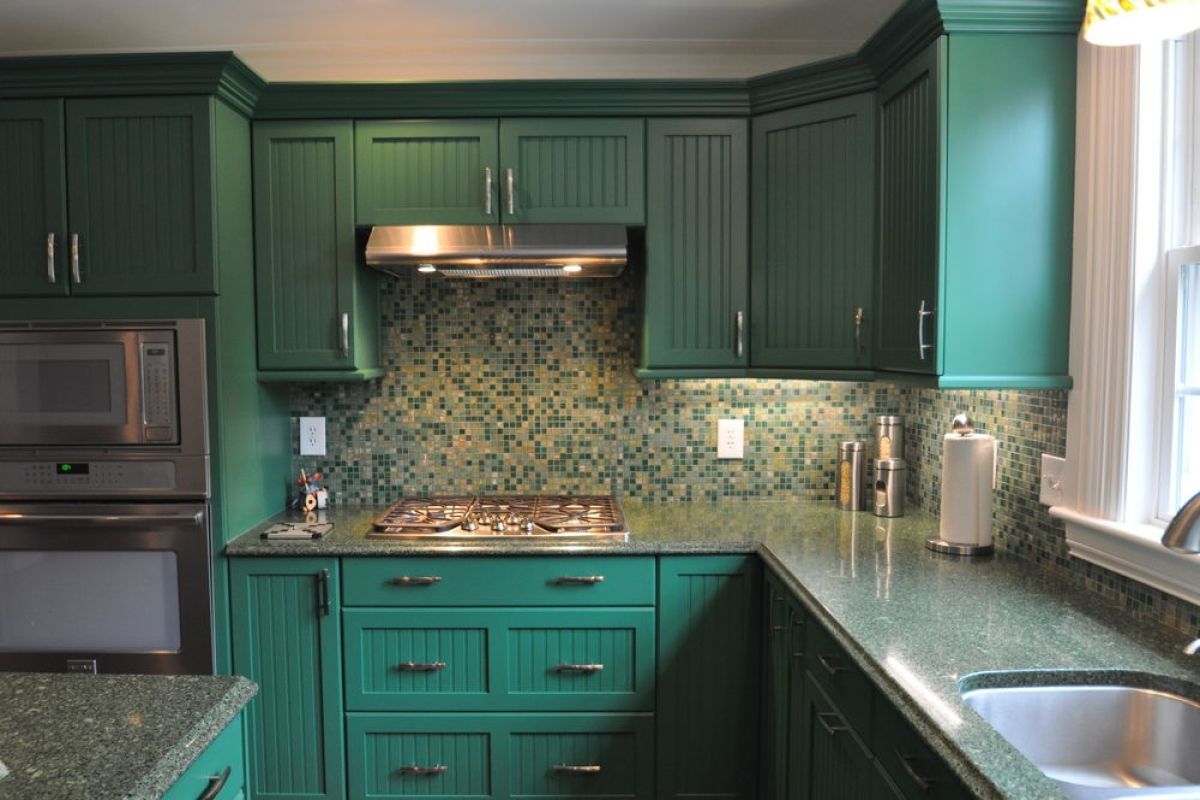 Green kitchen with mosaic tile backsplash, stainless appliances, and a window above the sink