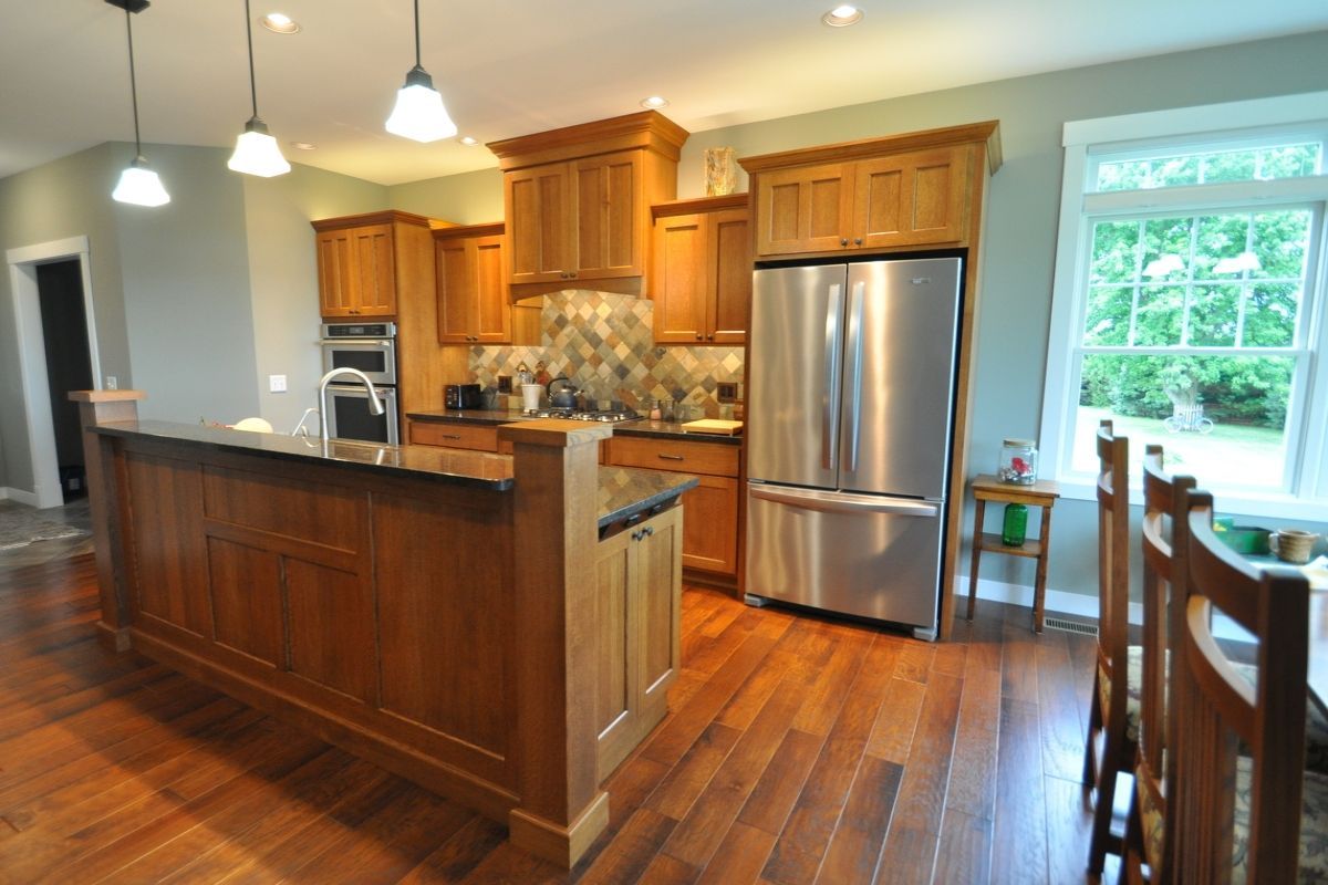 Warm wood kitchen with island, stainless steel fridge, hanging lights, and dining area by a bright window