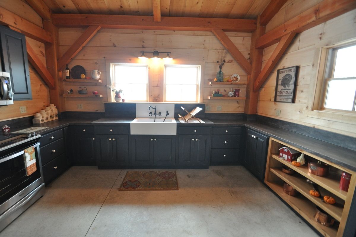 Rustic kitchen with dark cabinets, farmhouse sink, wood ceiling, and windows on both sides.