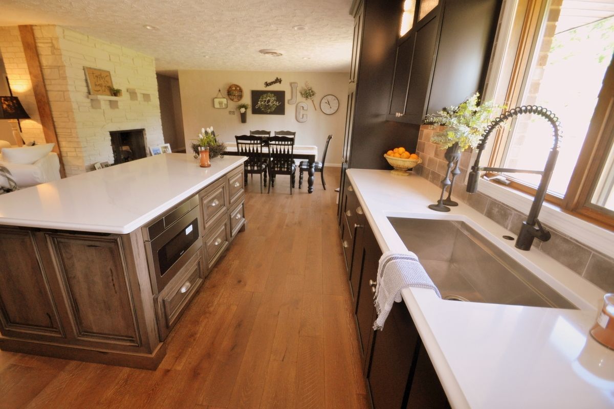 Bright kitchen with white island, wood floors, dining area, and large windows letting in natural light