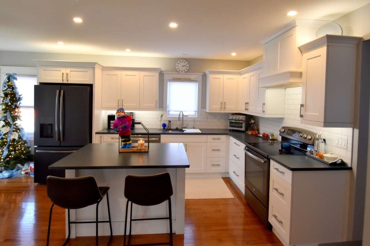 Bright modern kitchen with black island stools, white cabinets, stainless appliances, and hardwood floors