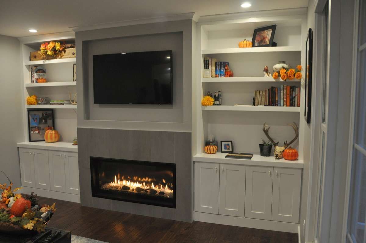 Built-in living room wall with TV, fireplace, and white shelving with autumn decor