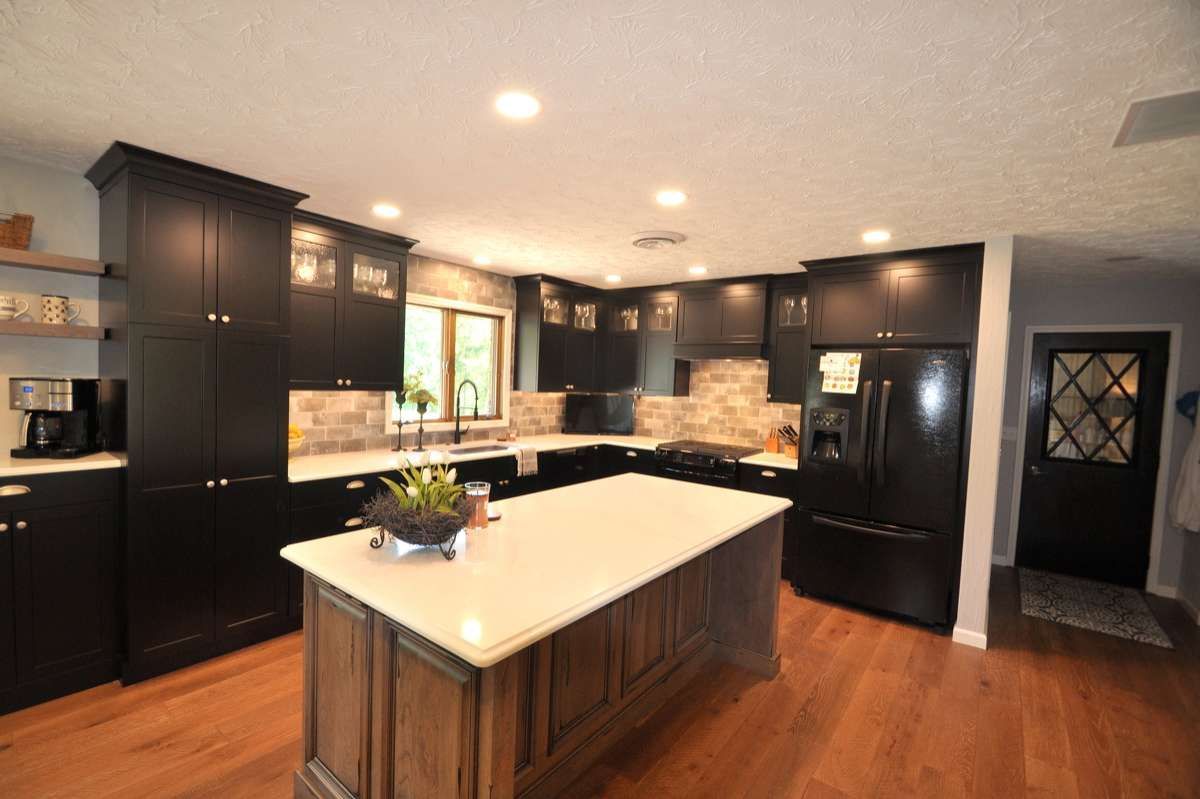 Modern black kitchen with a white island, wood floors, and recessed ceiling lights