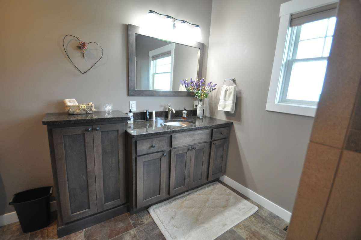 Modern bathroom vanity with gray cabinets, mirror, sink, towels, and a window beside a beige rug
