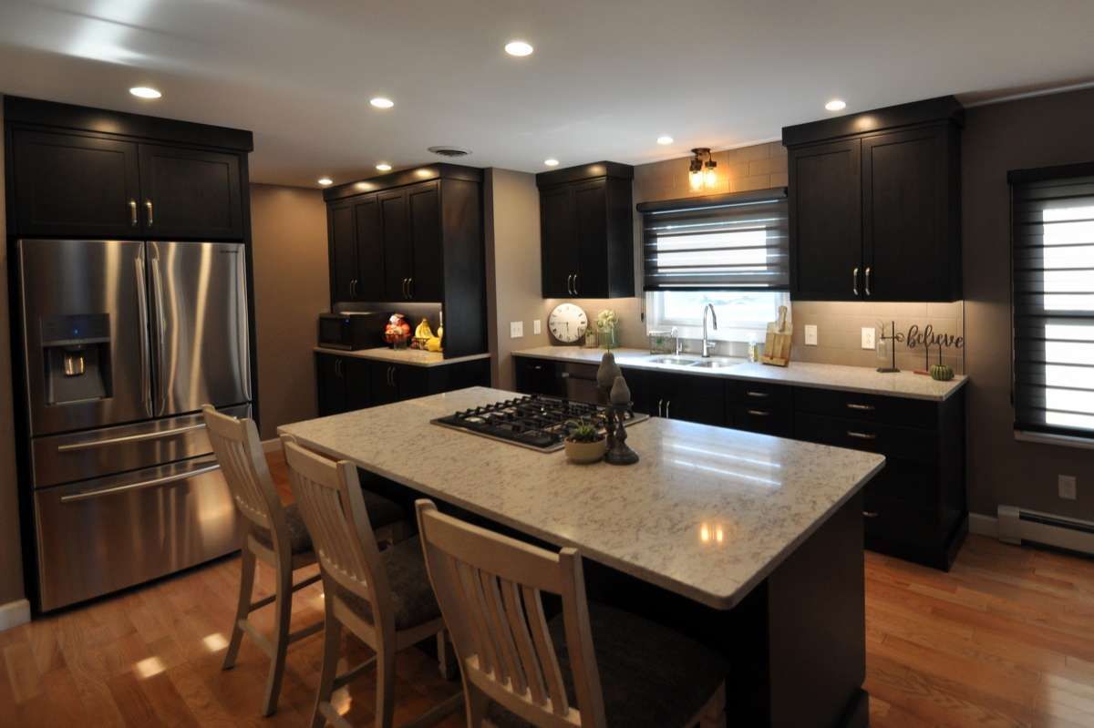 Modern kitchen with stainless steel appliances, dark cabinets, and a granite island under recessed lighting