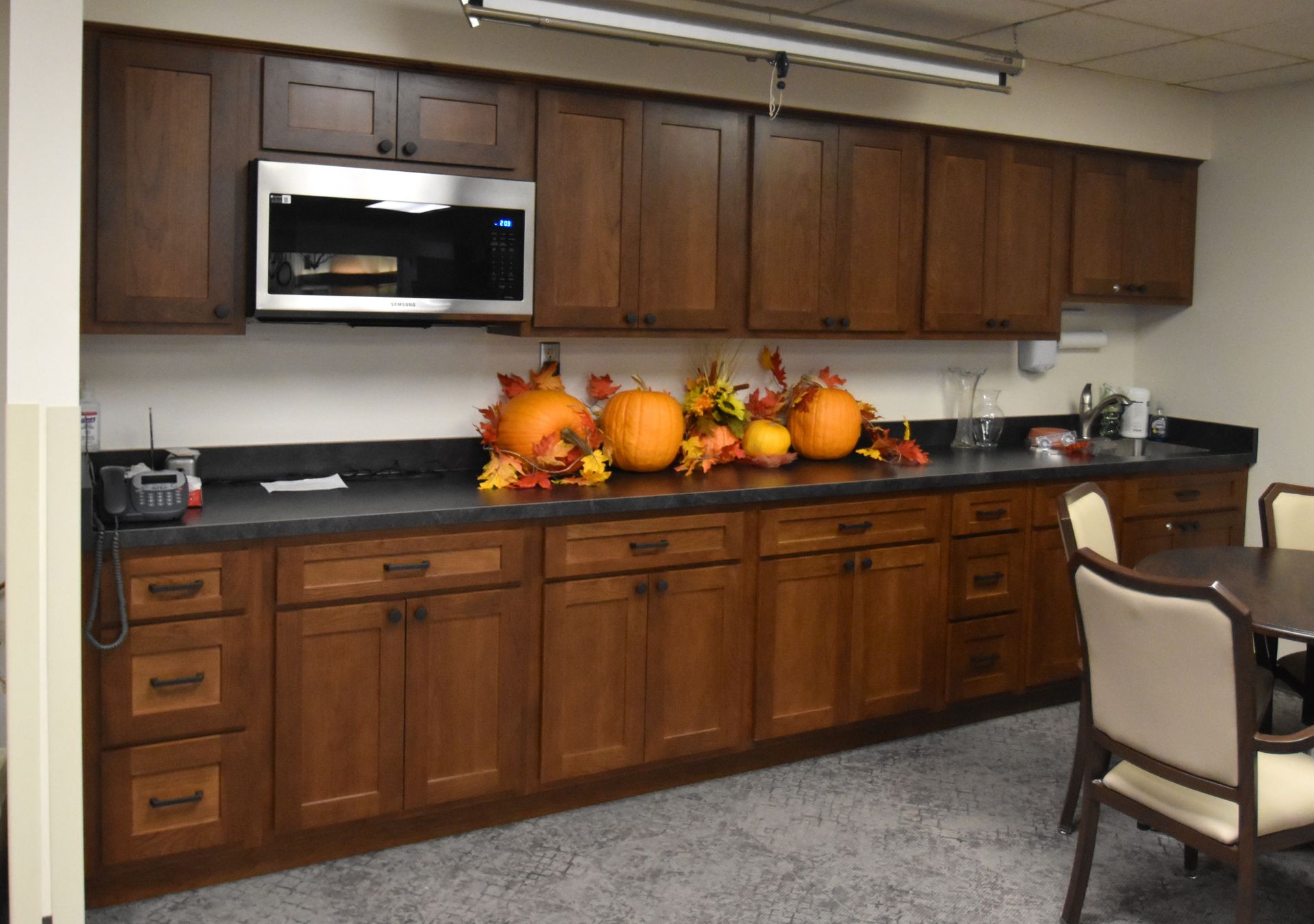 Office kitchenette with wooden cabinets, sink, and autumn pumpkin centerpiece on the counter