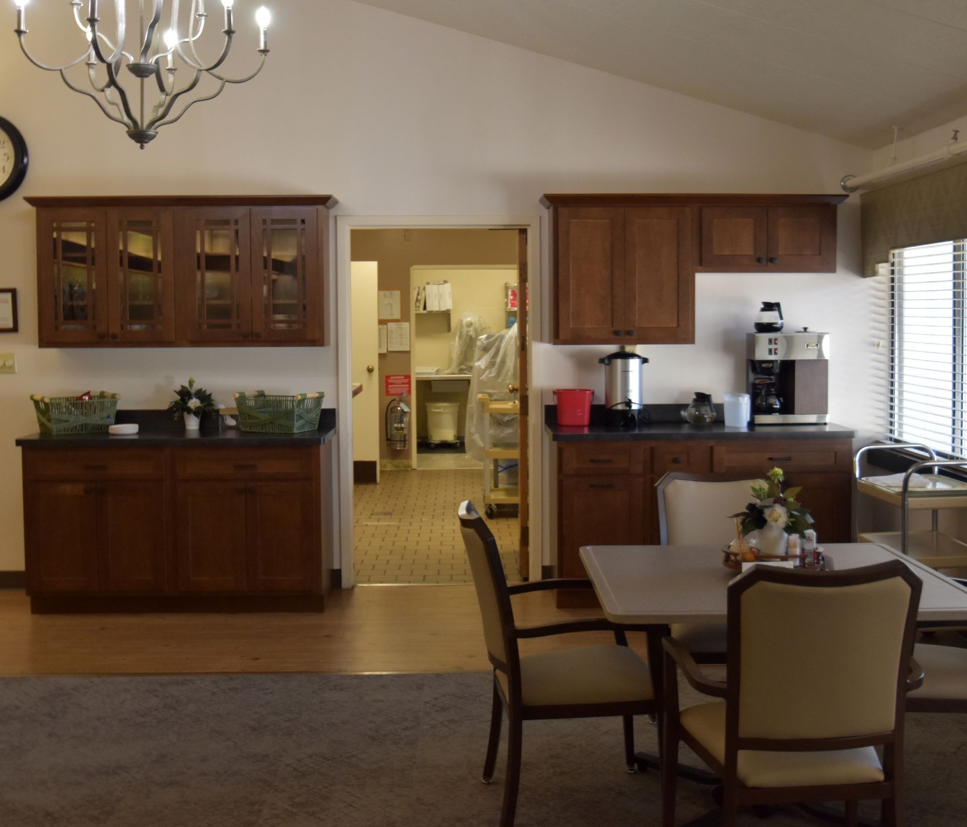 Dining room and kitchen with wood cabinets, chandelier, and table set near a bright window.