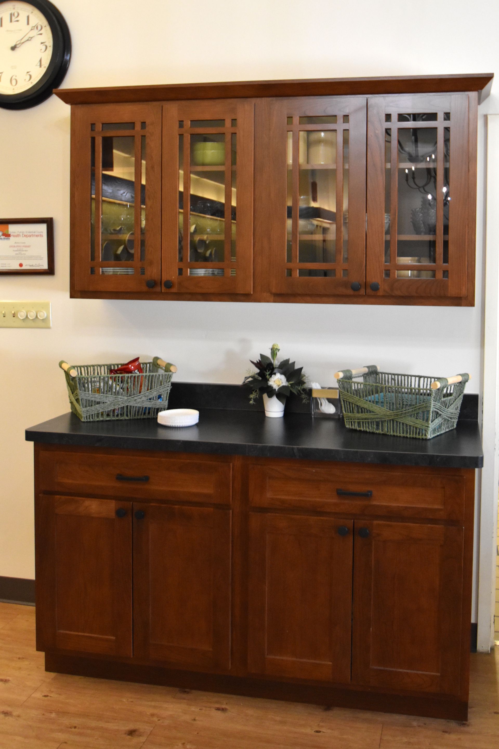 Wooden cabinet with glass-front hutch and black countertop holding baskets and decor in a room